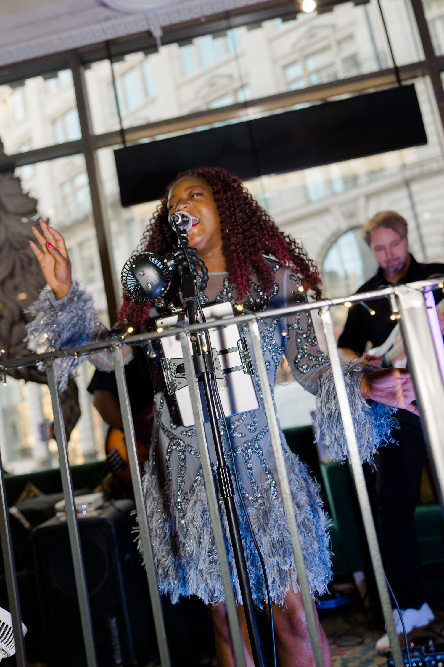 Female singer in silver sequined dress performing at microphone during wedding reception.