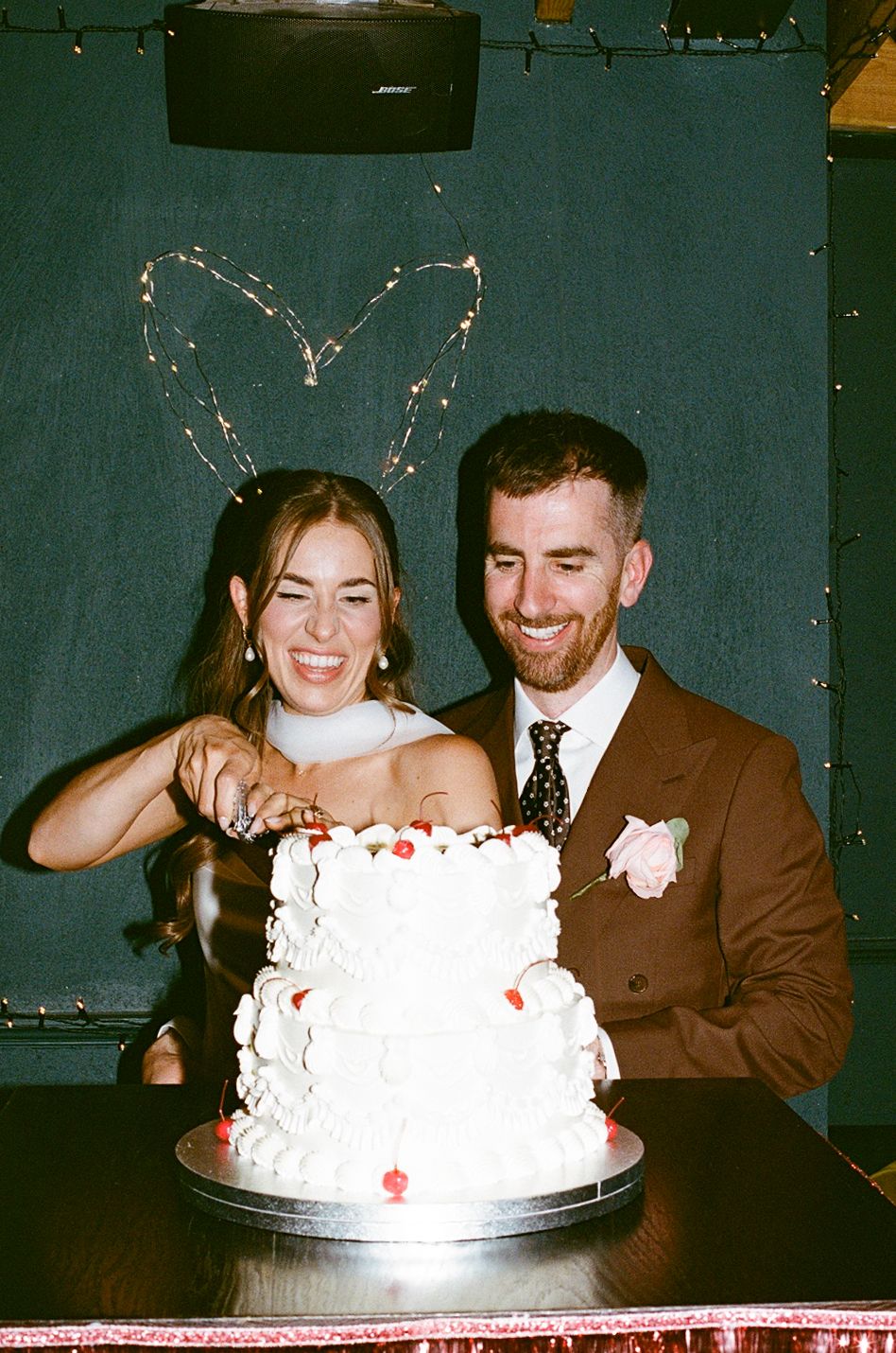 Smiling bride and groom cutting a two-tier white wedding cake decorated with strawberries and cream.