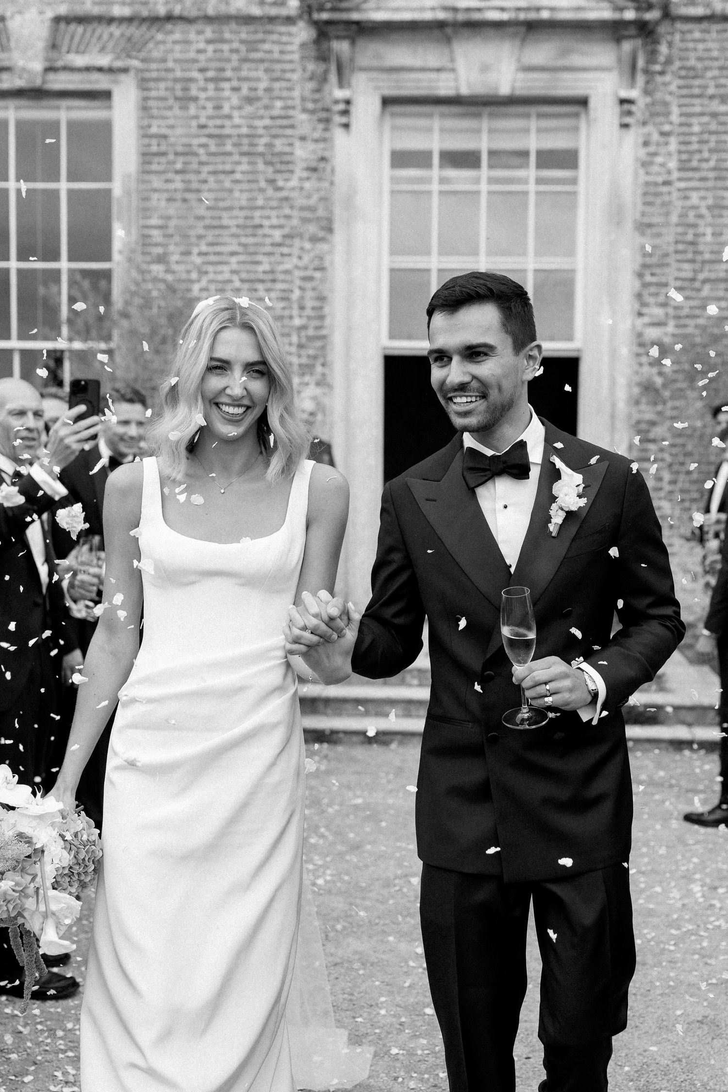 Newlyweds celebrating with champagne and confetti outside a Georgian brick manor house.