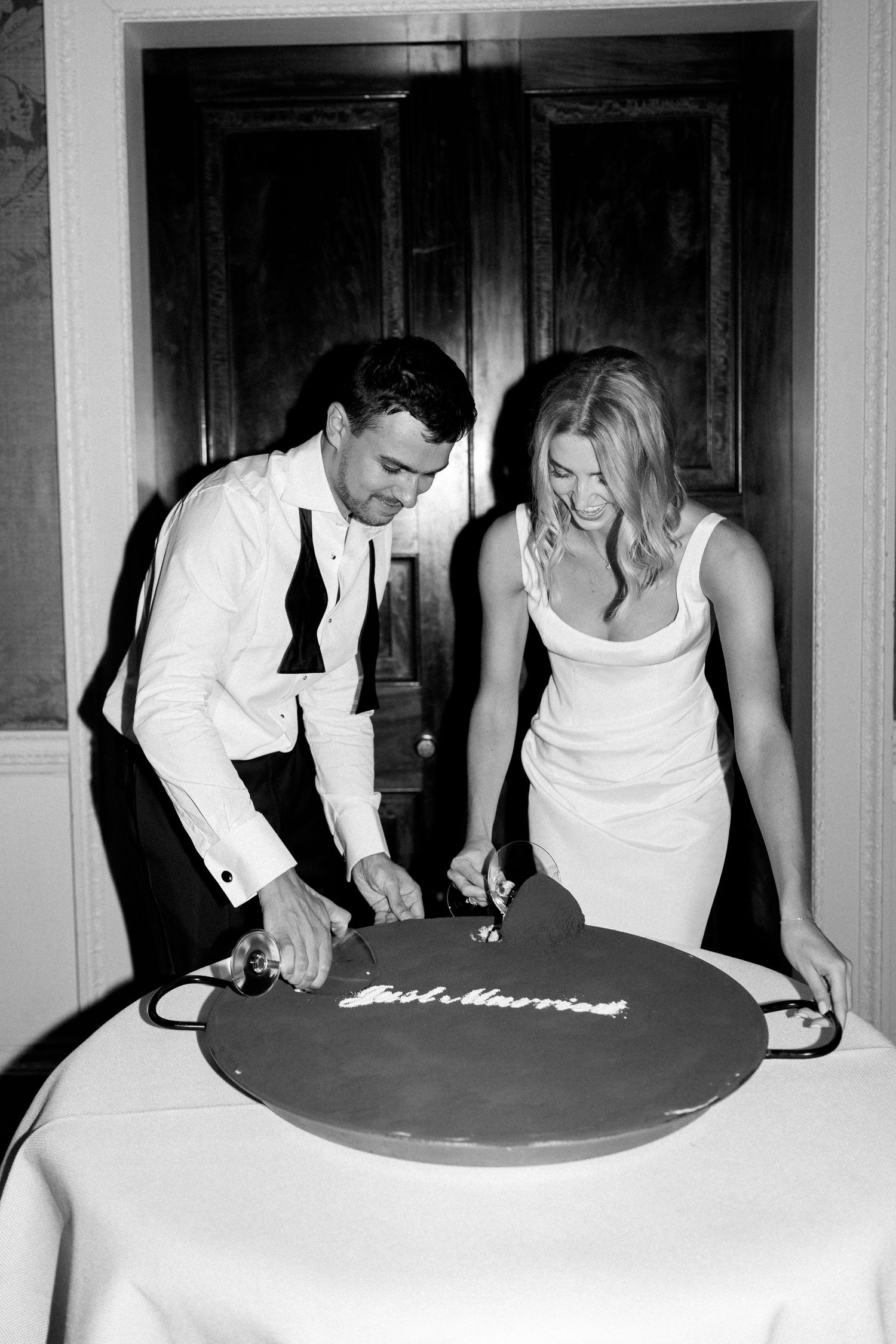 Newlyweds cut round Just Married cake in black and white wedding reception photo.