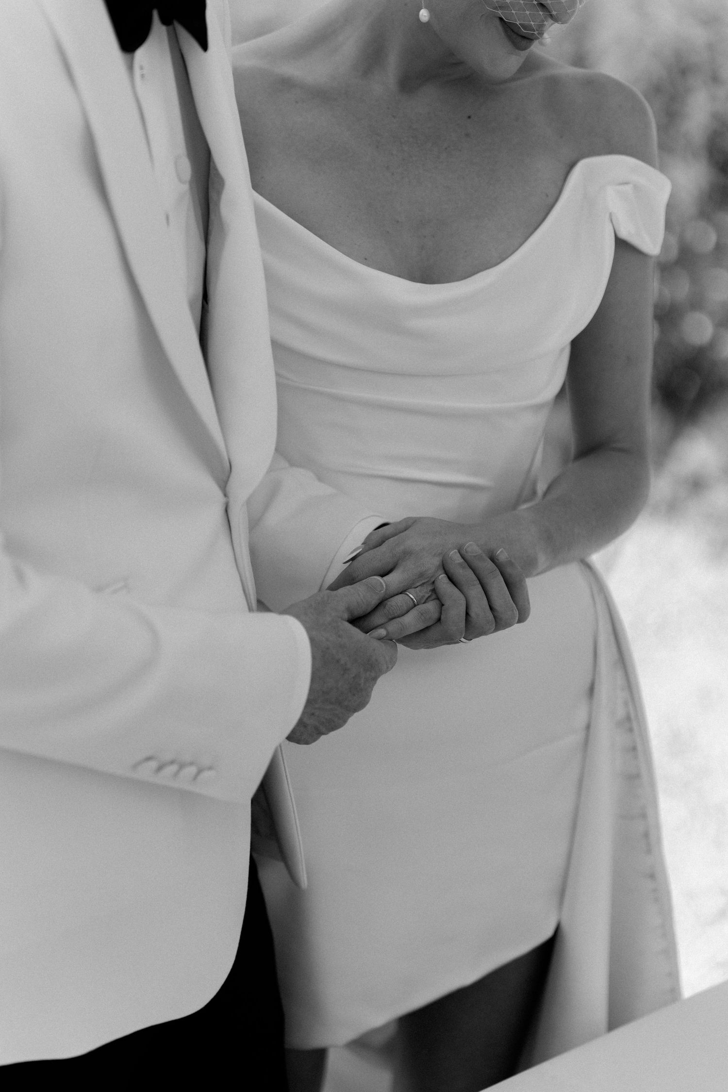 Black and white close-up of a bride and groom holding hands during their wedding ceremony.