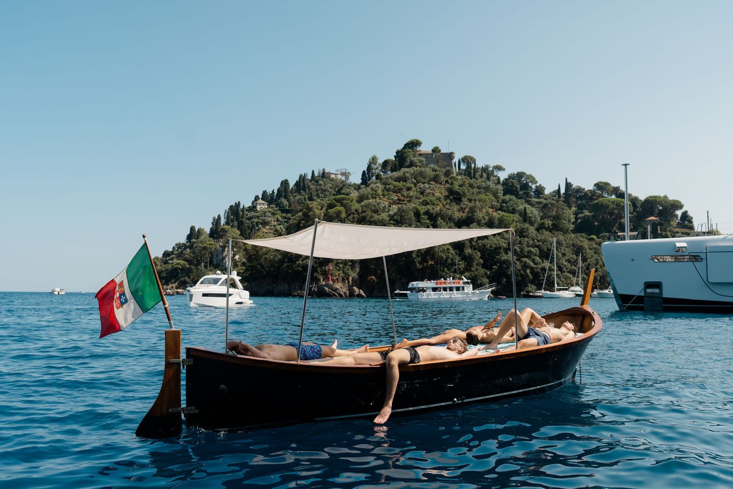 Classic Italian wooden boat with Italian flag anchored near a lush green island in Portofino.