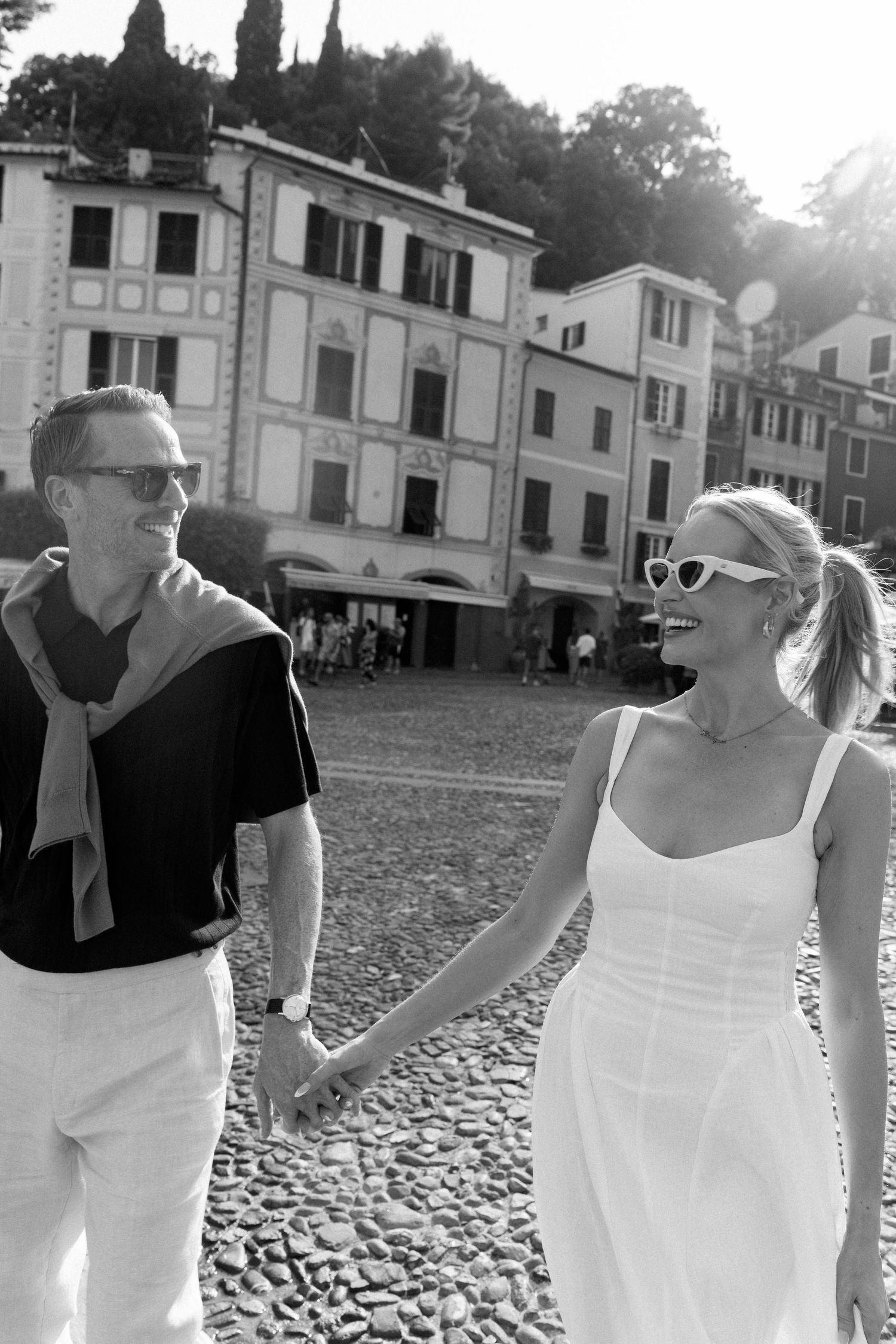 Happy couple holding hands and walking through a cobblestone square in Portofino, Italy.
