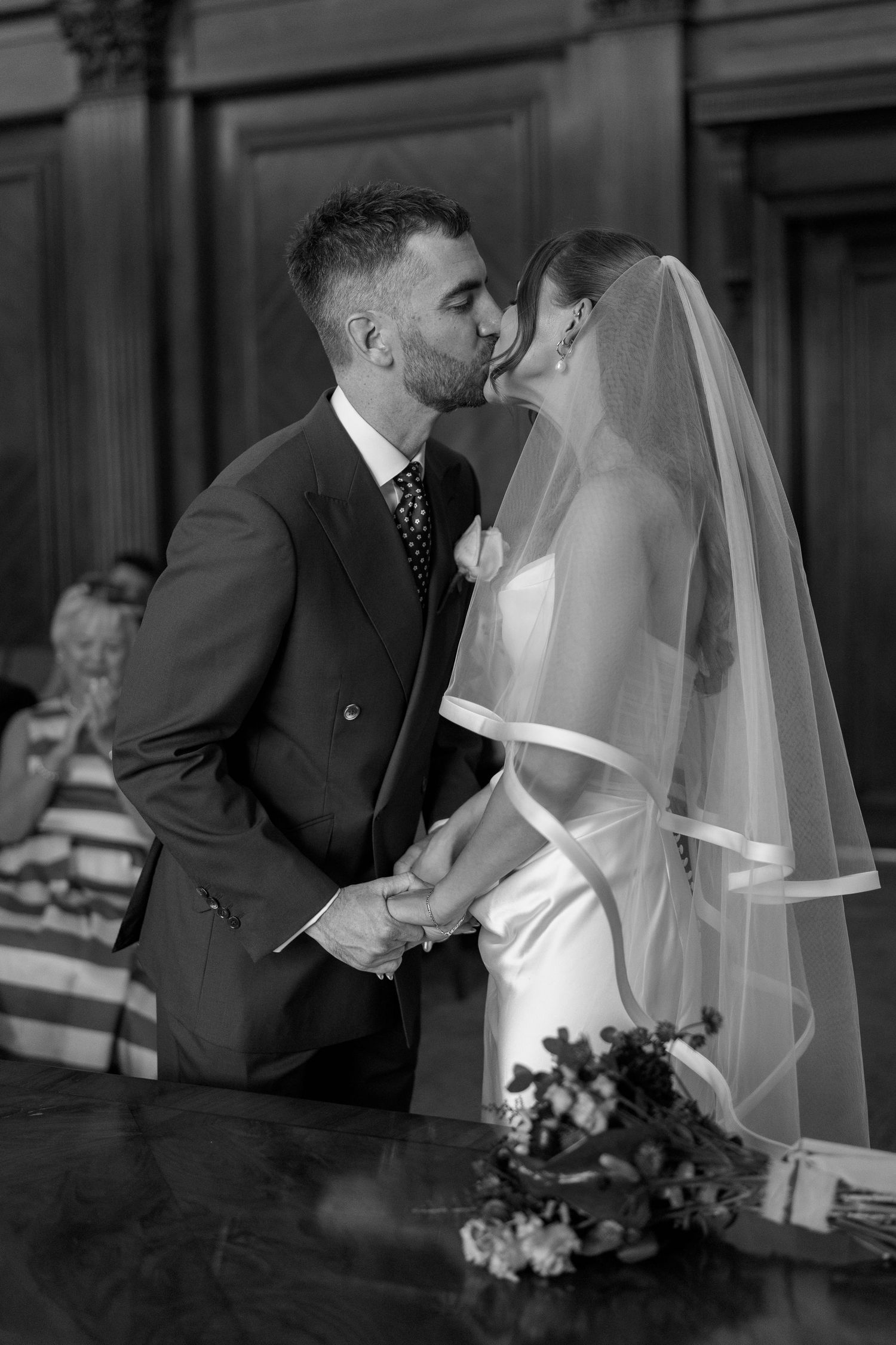 Bride and groom share first kiss at altar during wedding ceremony in black and white photo.