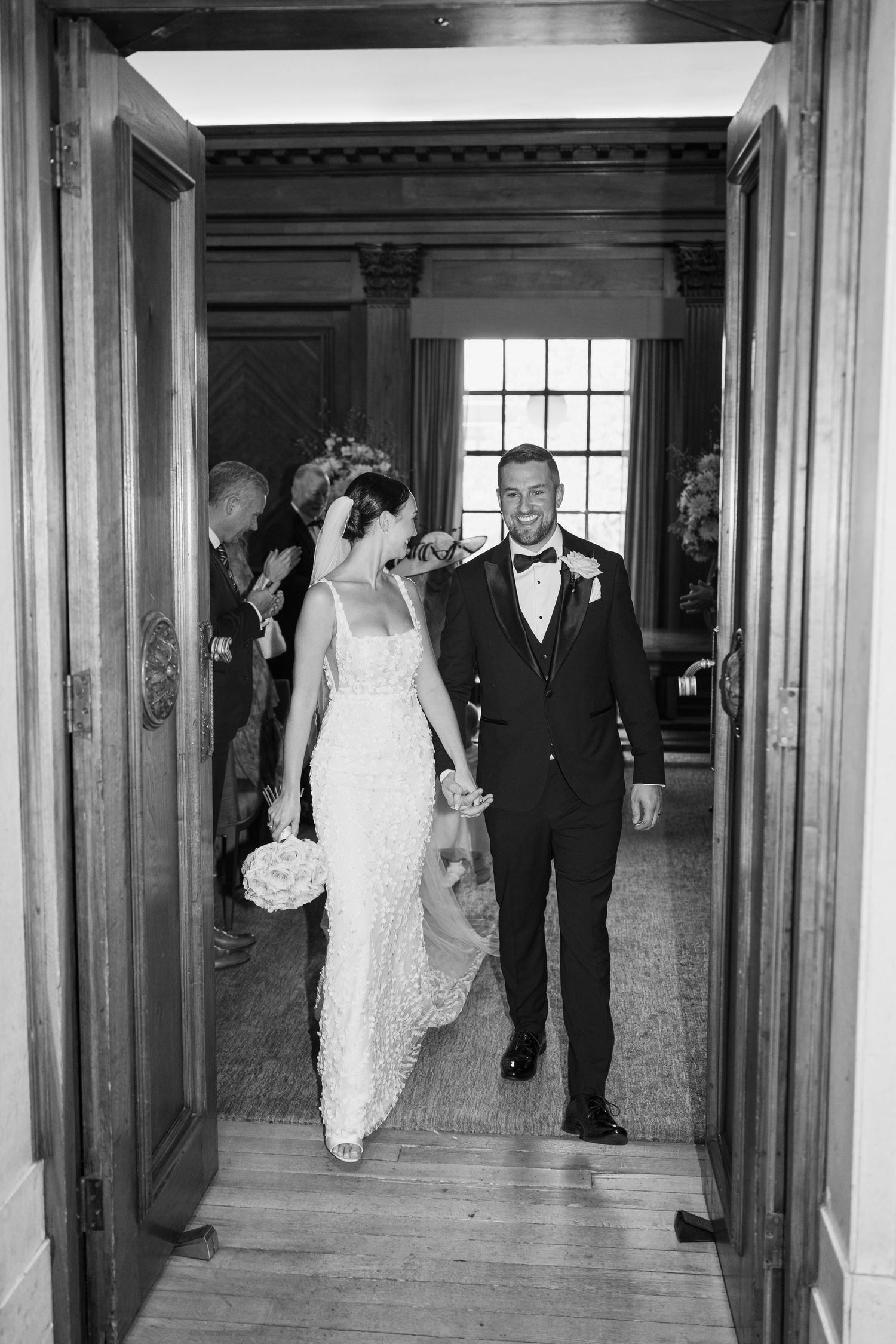 Wedding party walking through a grand hallway with wooden columns and paneling.