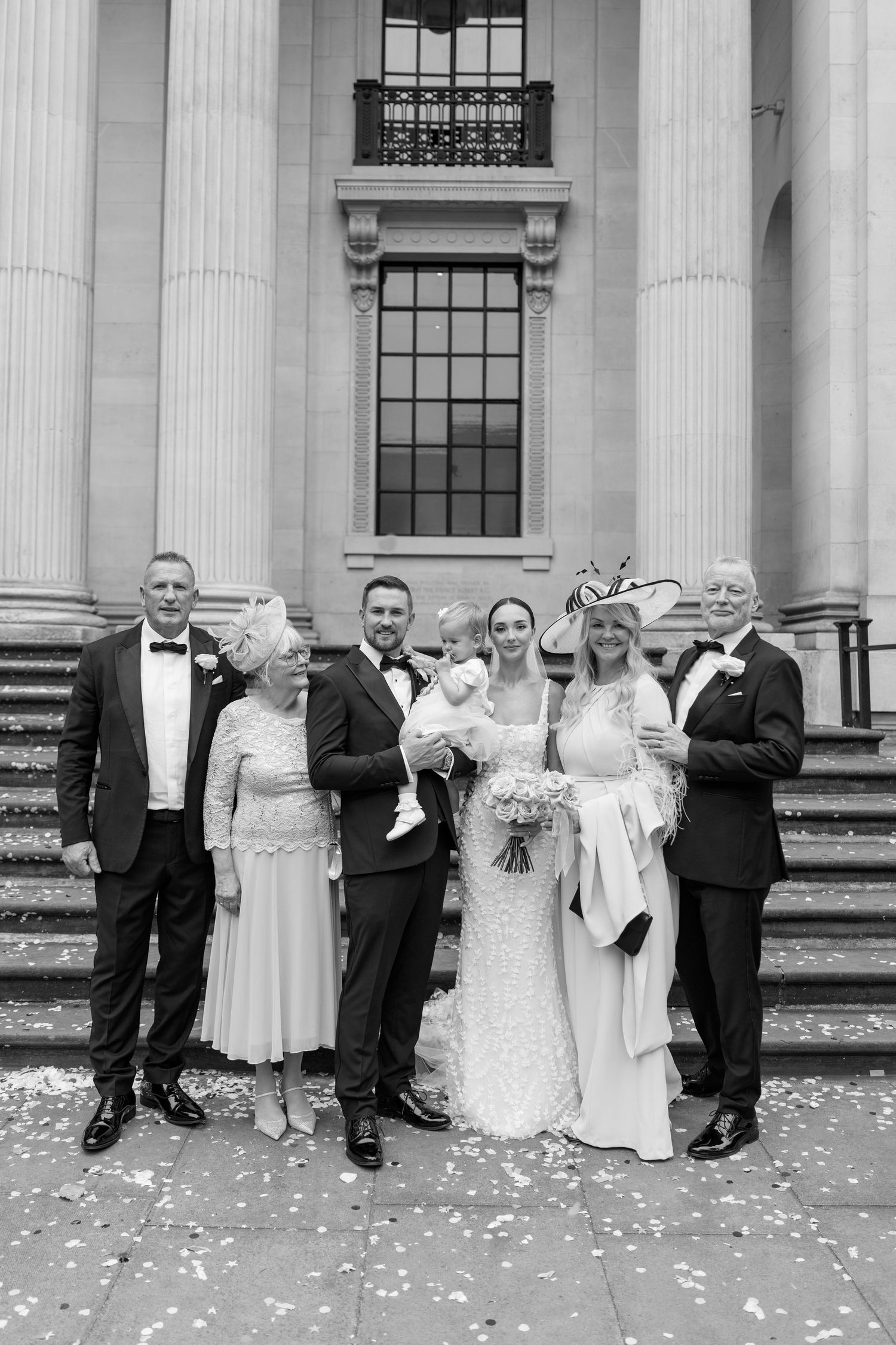 Wedding party poses on grand stone steps with flower petals scattered around them.