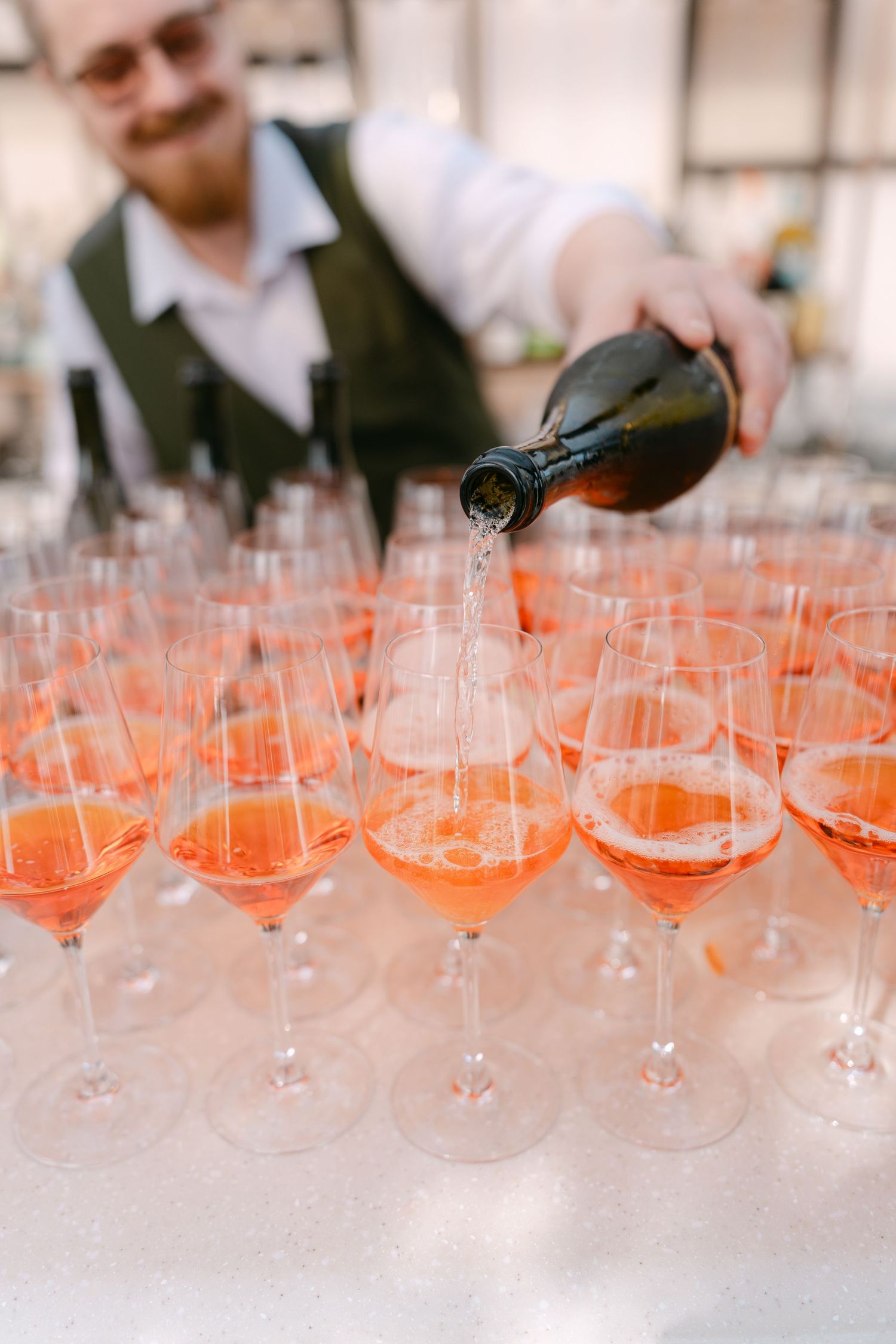 Bartender pouring champagne into multiple glasses at an event.