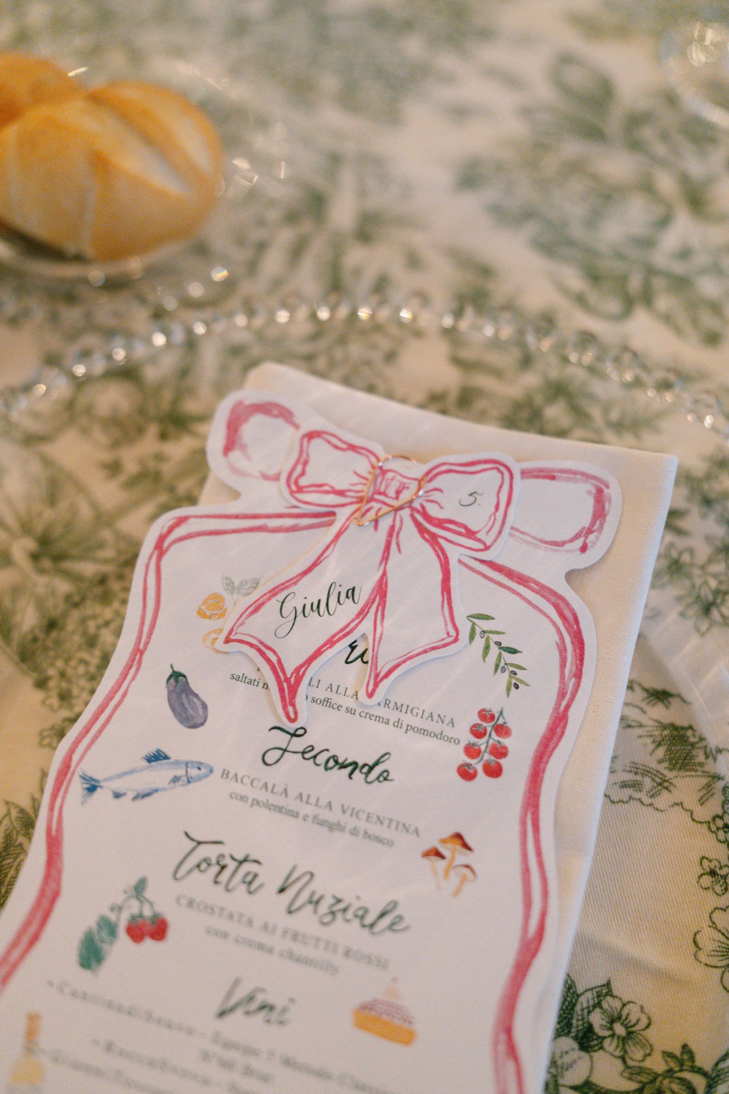 Wedding menu cards decorated with pink watercolor bows and floral designs lay on a patterned tablecloth.