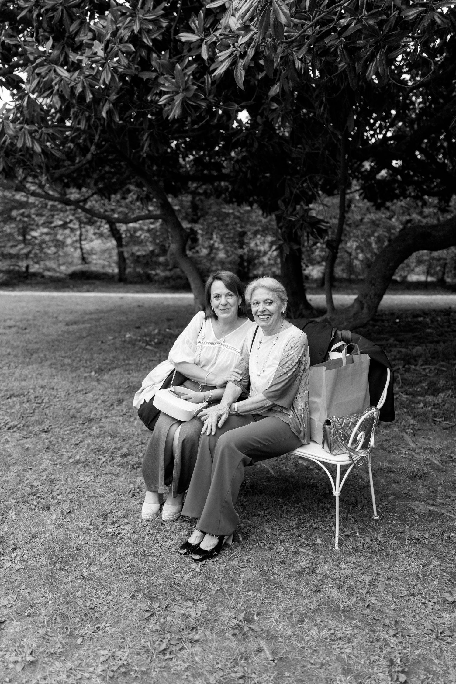 Guests seated on chairs under trees at an outdoor gathering.