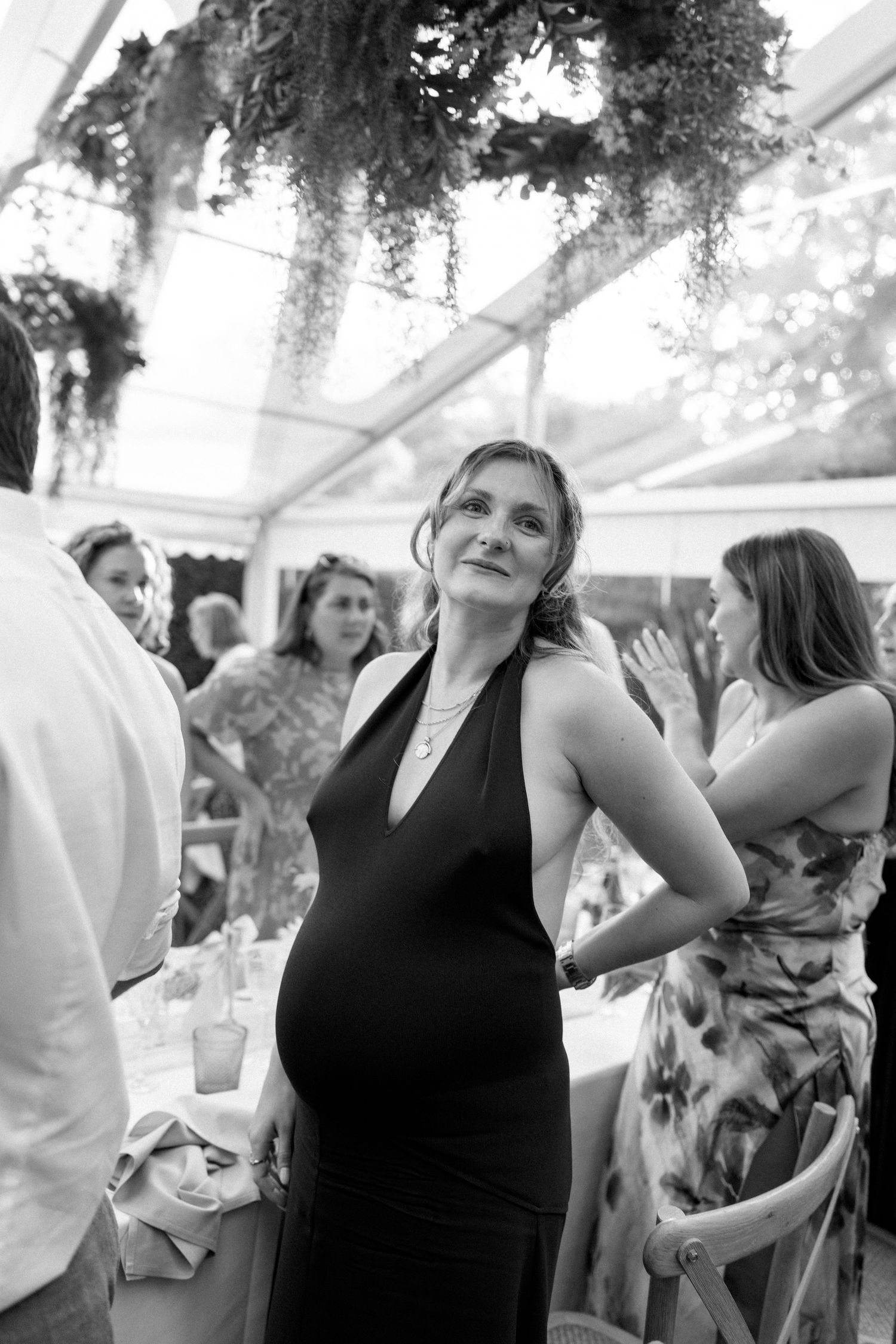Guest in black dress dancing at wedding reception under tent with hanging greenery.