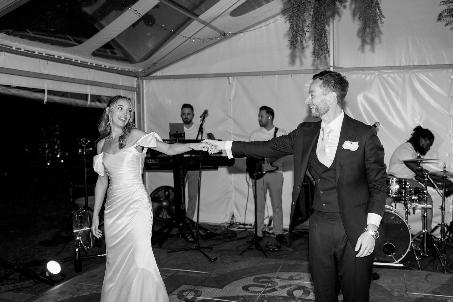 A couple performs their first dance on a patterned floor with a live band in the background.