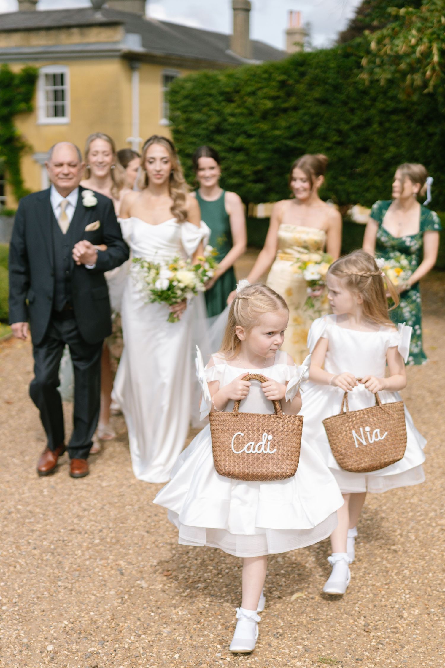 Wedding processional on gravel path with flower girls carrying personalized baskets.