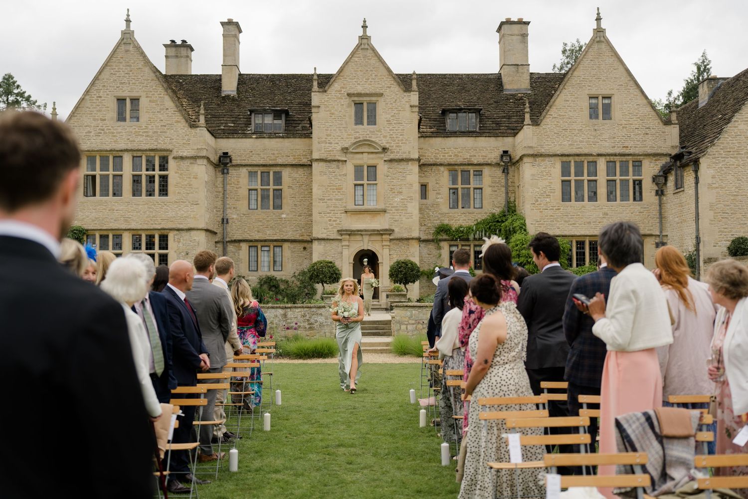 Outdoor wedding ceremony on manicured lawn before a grand English manor house.