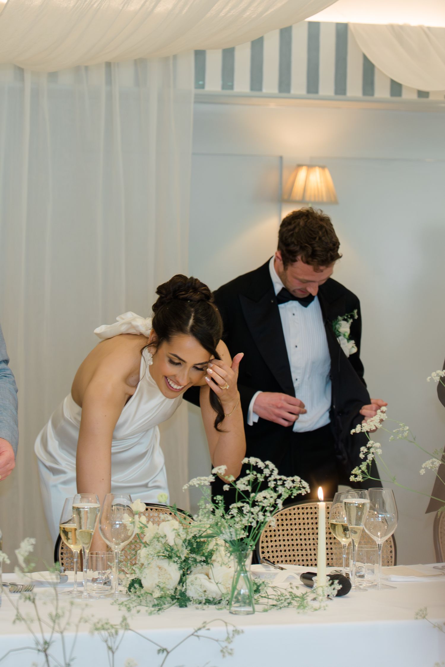 Bride and groom laughing together at decorated head table during wedding reception.