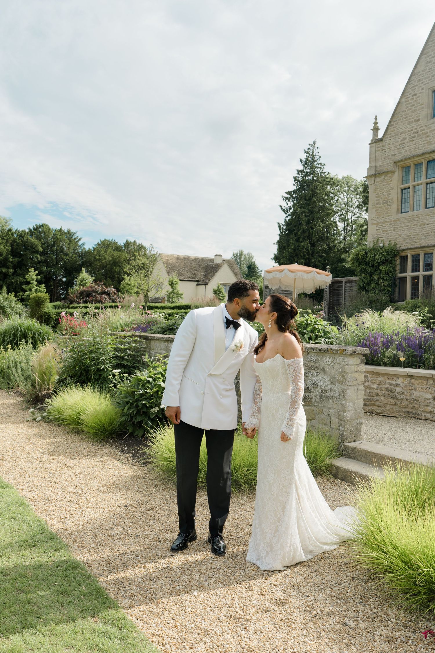 Bride and groom share a romantic moment in lush garden outside a beautiful stone manor.