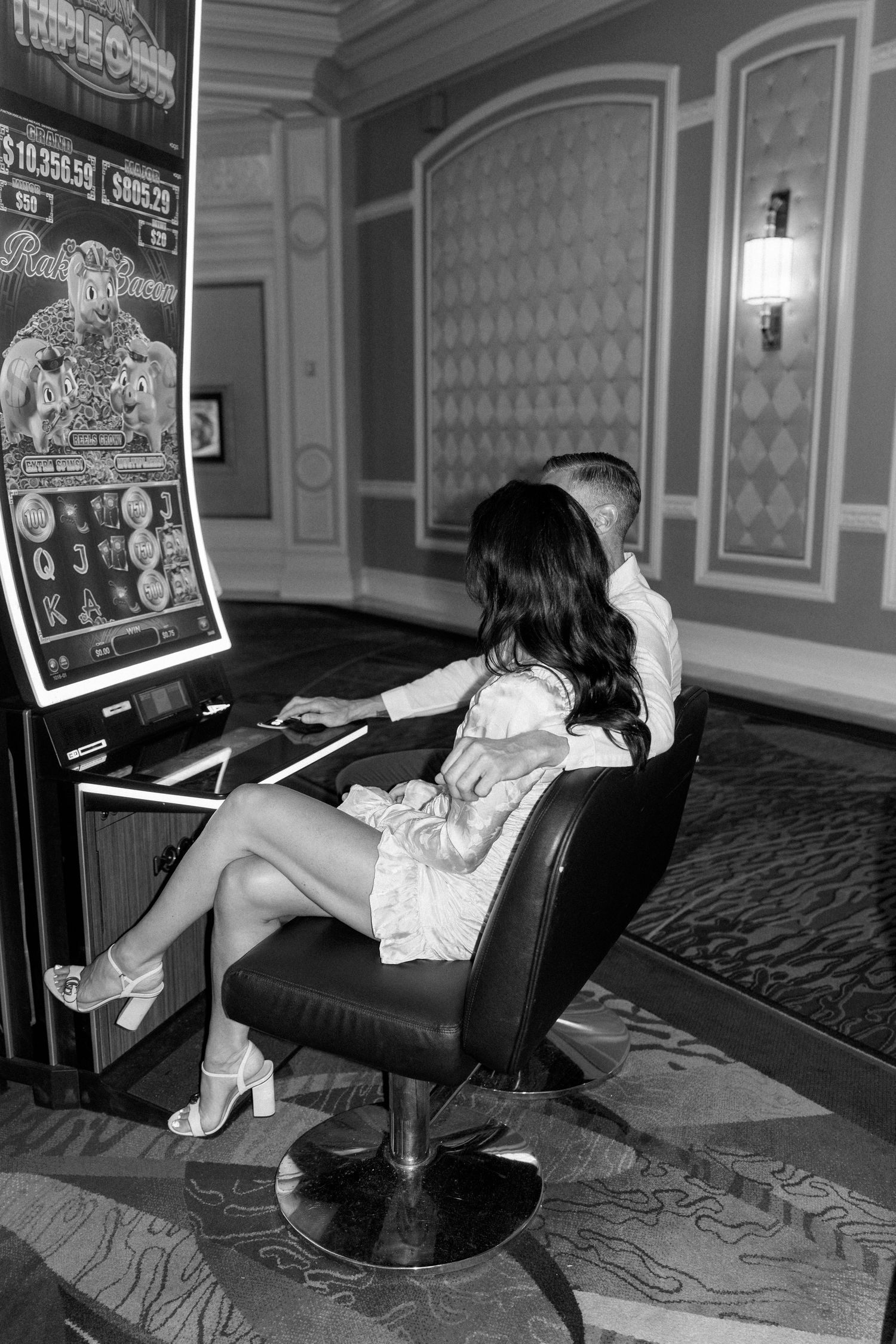 A couple plays a slot machine in formal attire at a casino.