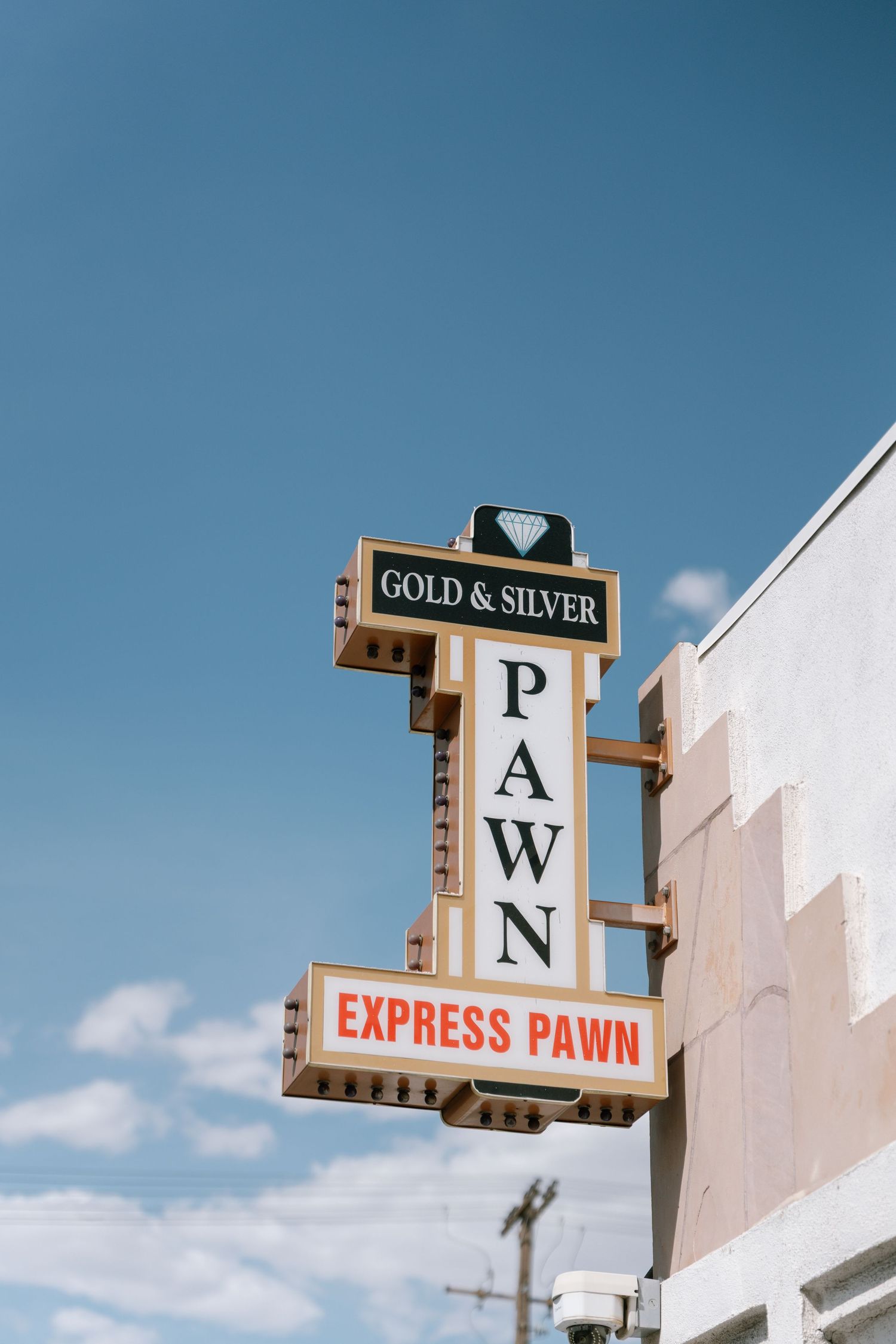 Vertical pawn shop signage against a bright blue sky in an urban setting.