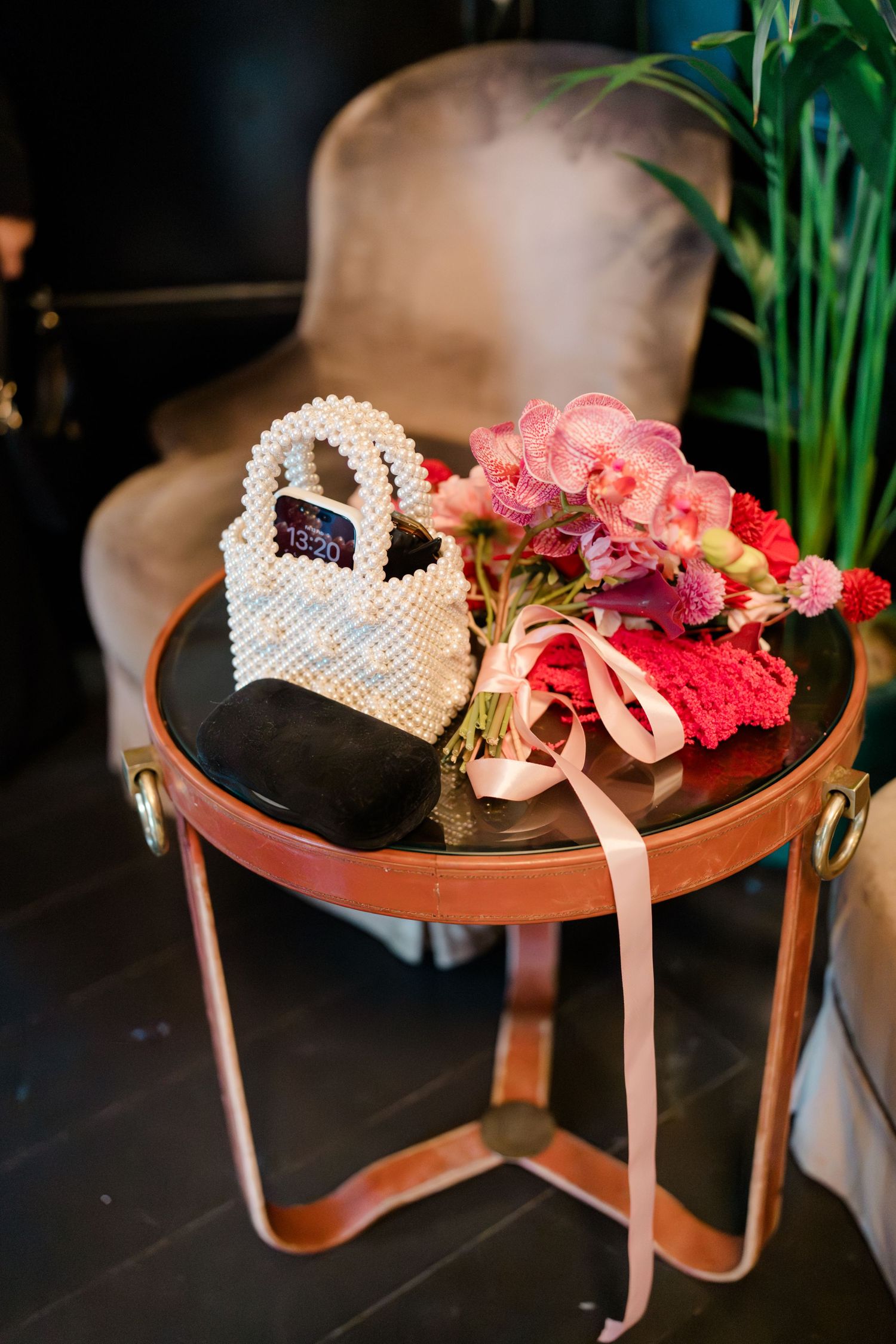 Wedding accessories including pearl beaded bag, black heels, and pink floral bouquet on side table.
