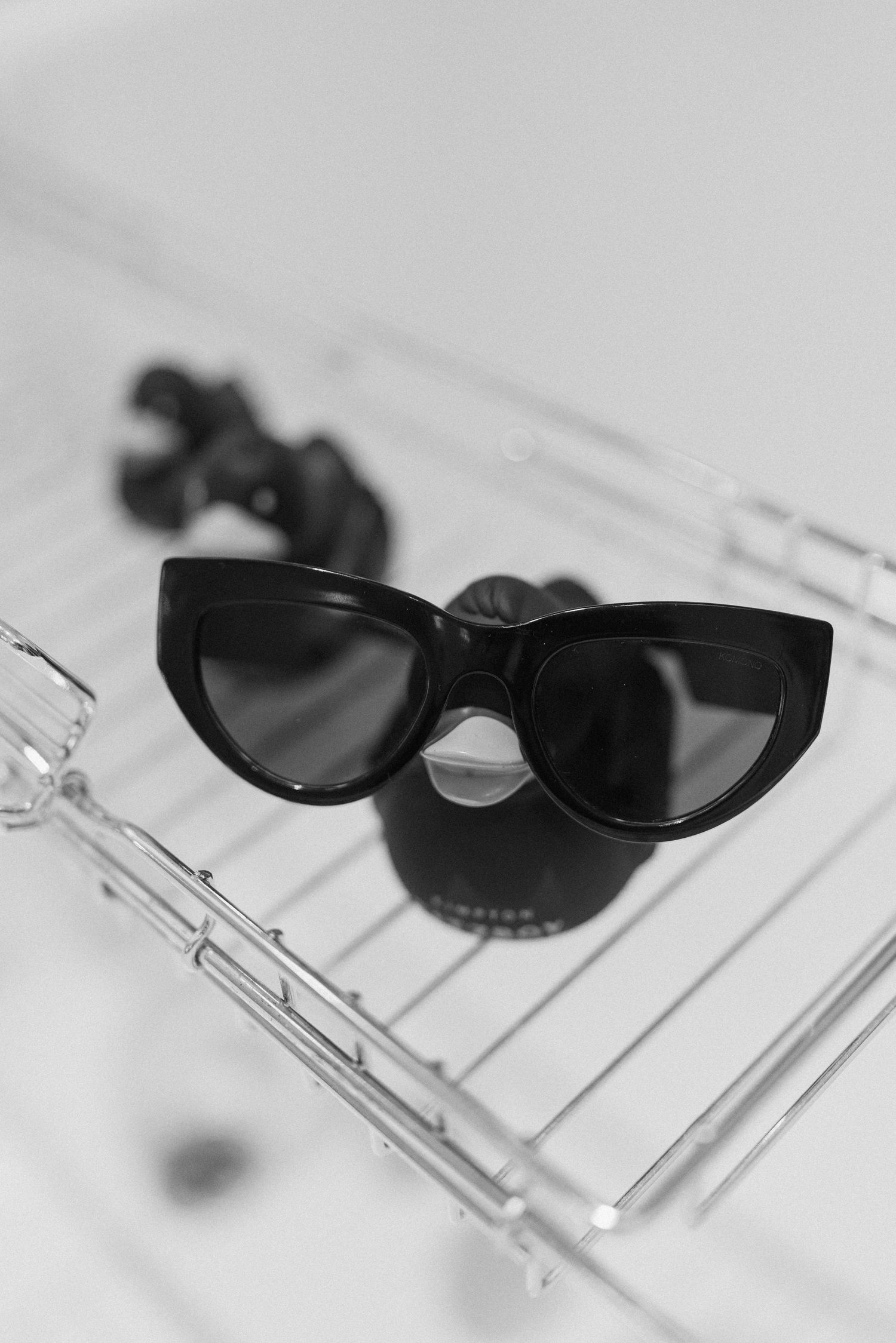 Black cat-eye sunglasses resting on gold bath caddy in black and white photo.