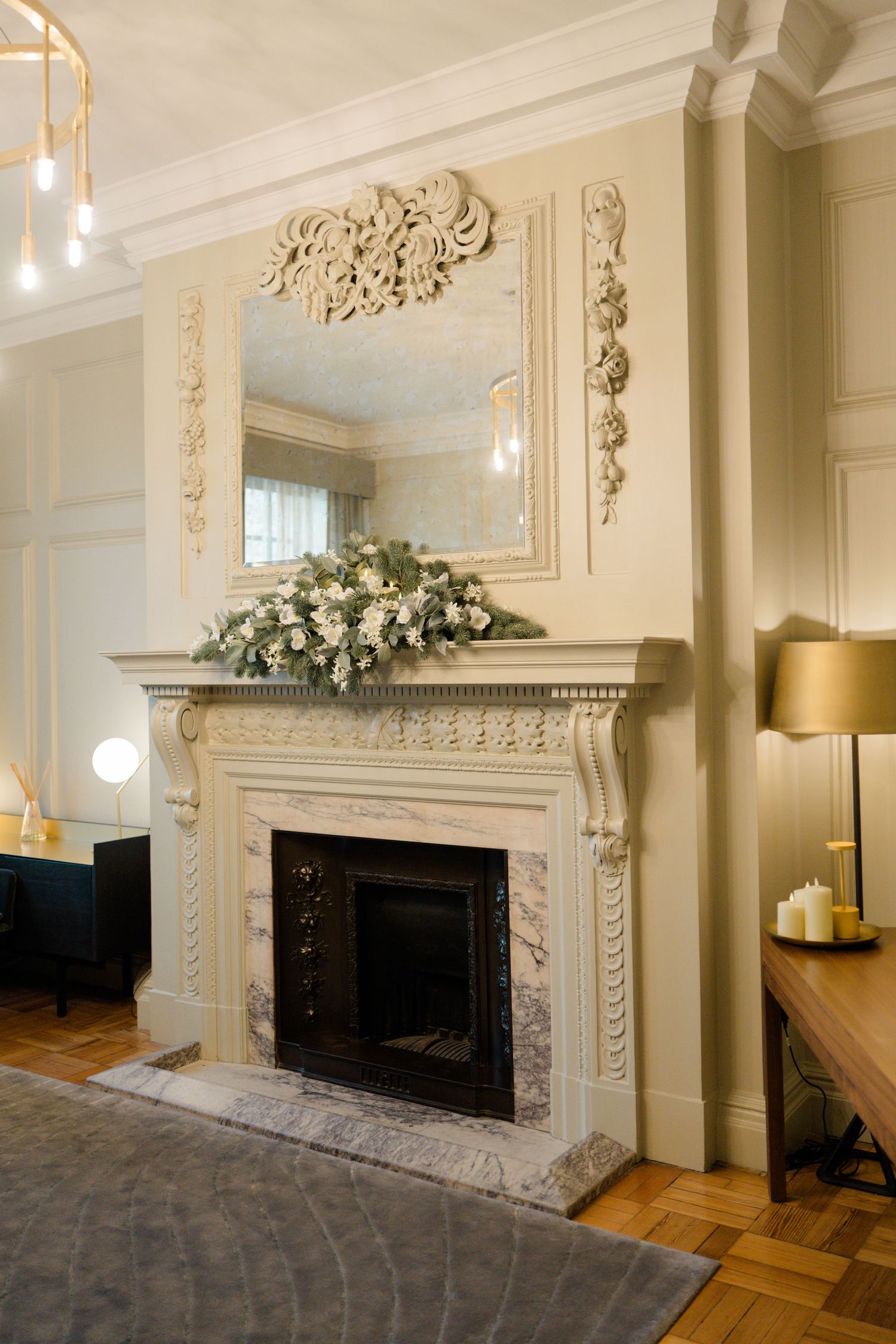 Elegant white marble fireplace with ornate carved details, floral garland, and decorative mirror in a classic living room.