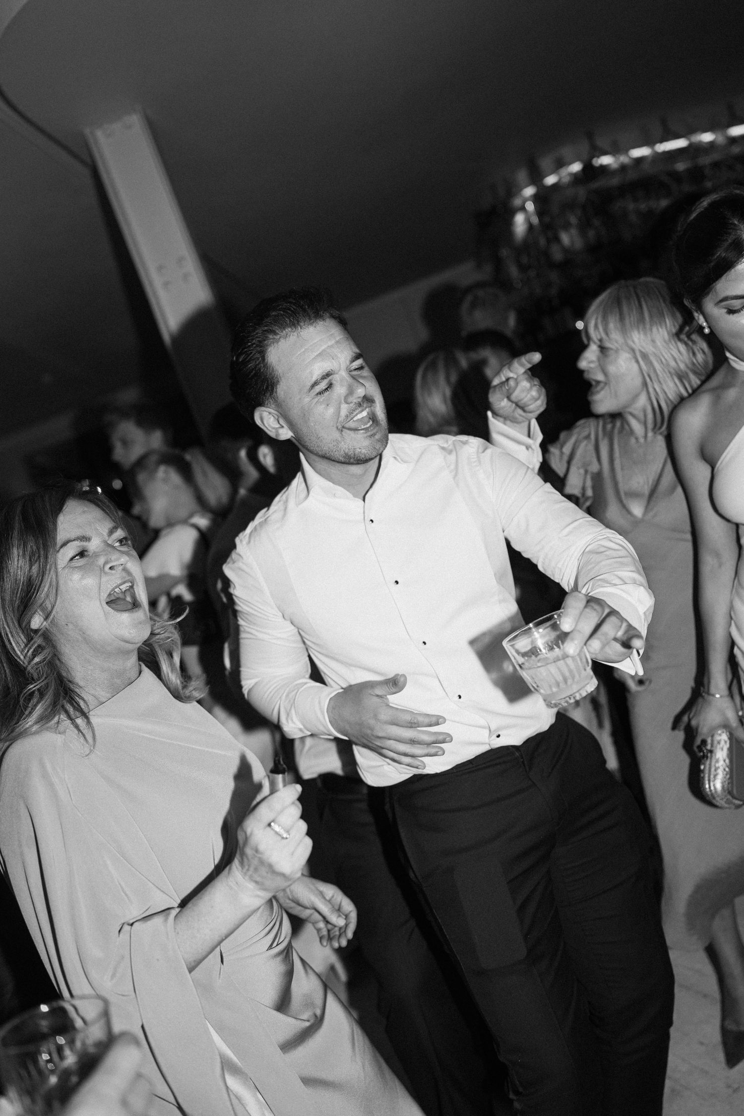 Black and white photo of wedding guests laughing and dancing together at a lively wedding reception party.