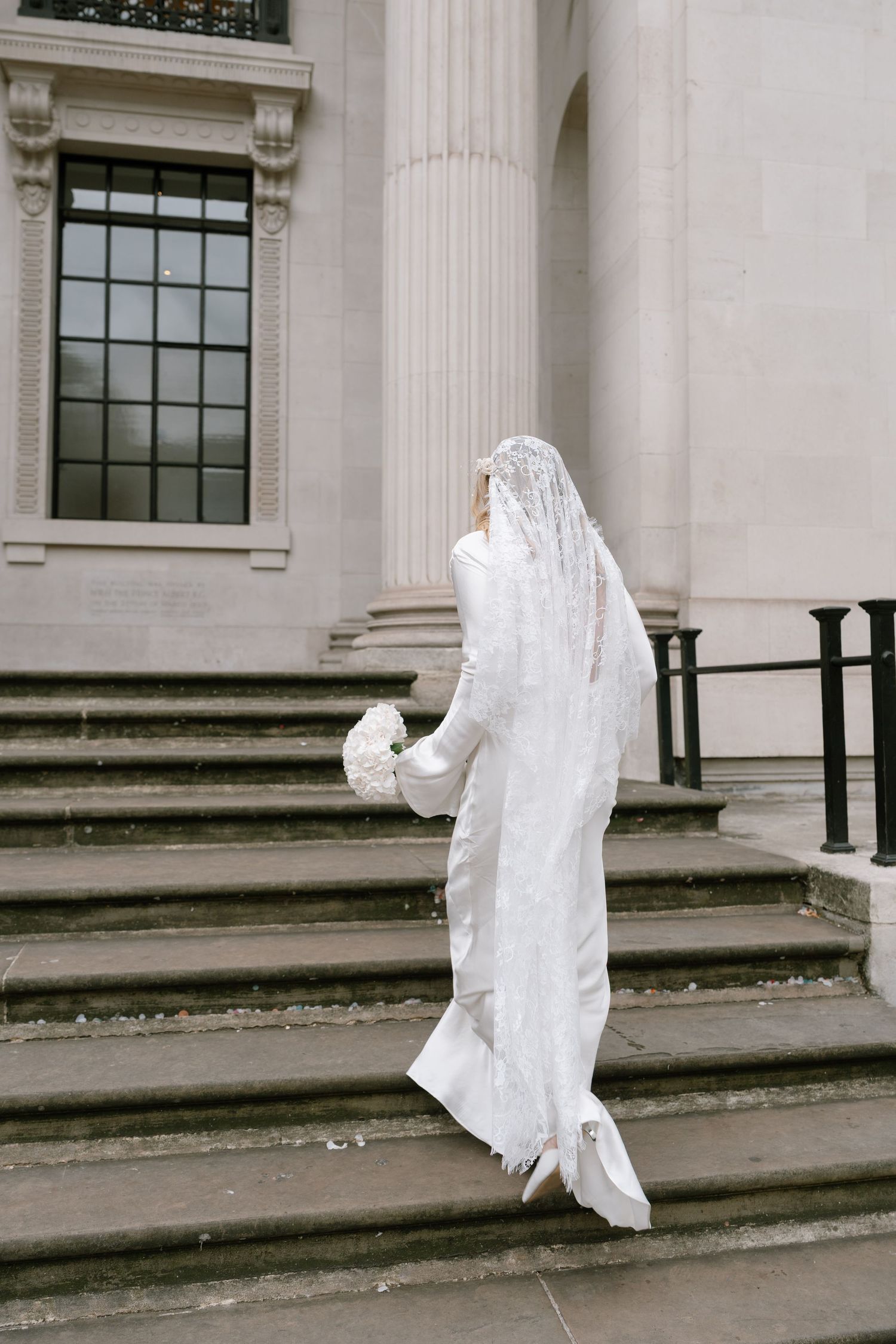 Sequence showing someone in a white dress ascending stone steps of a classical building.