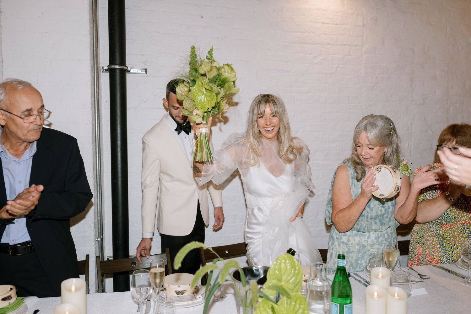 Wedding reception dinner table setting with white floral centerpieces and guests enjoying the celebration.