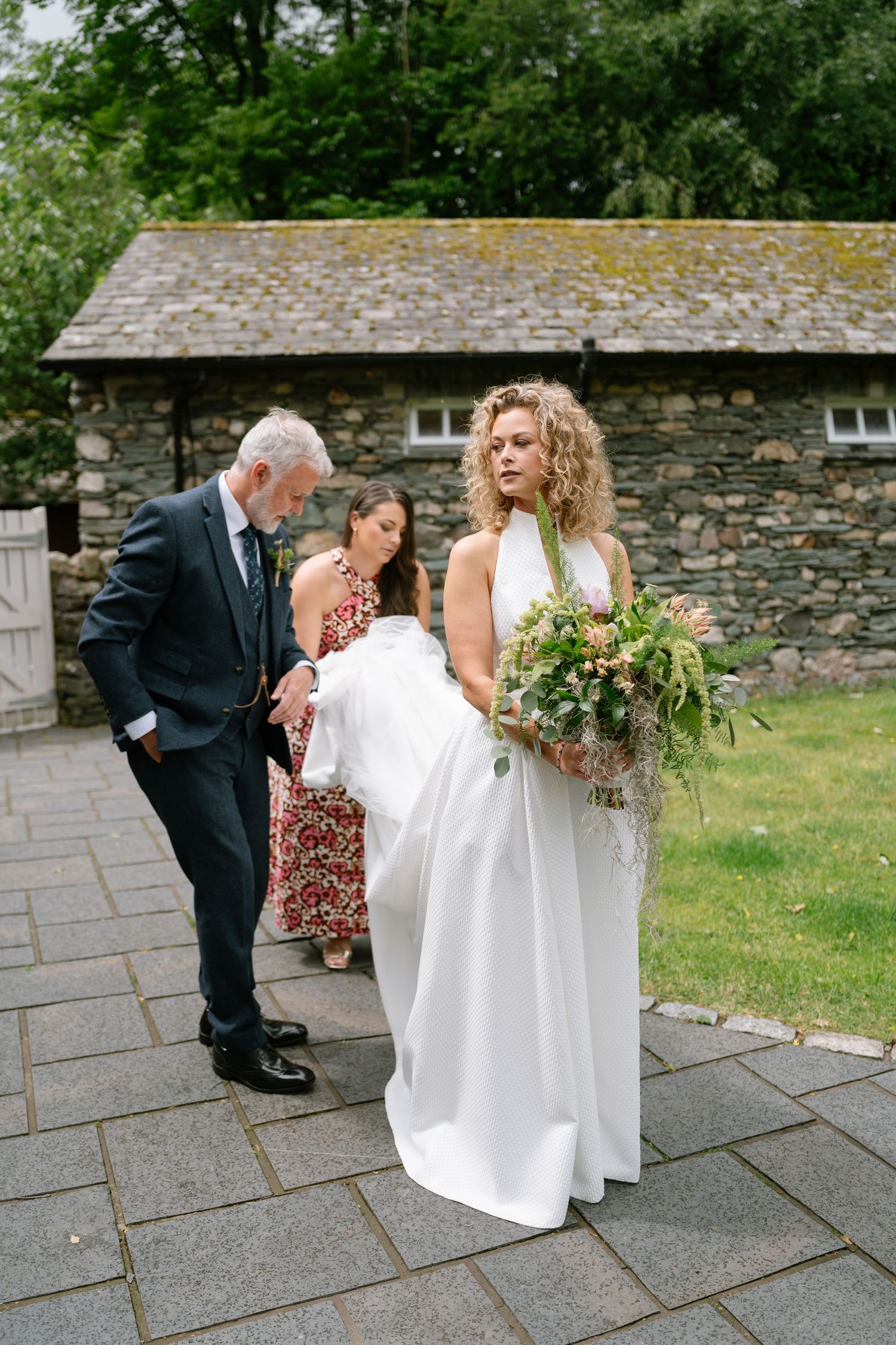 Wedding party gathered on stone patio outside rustic building.