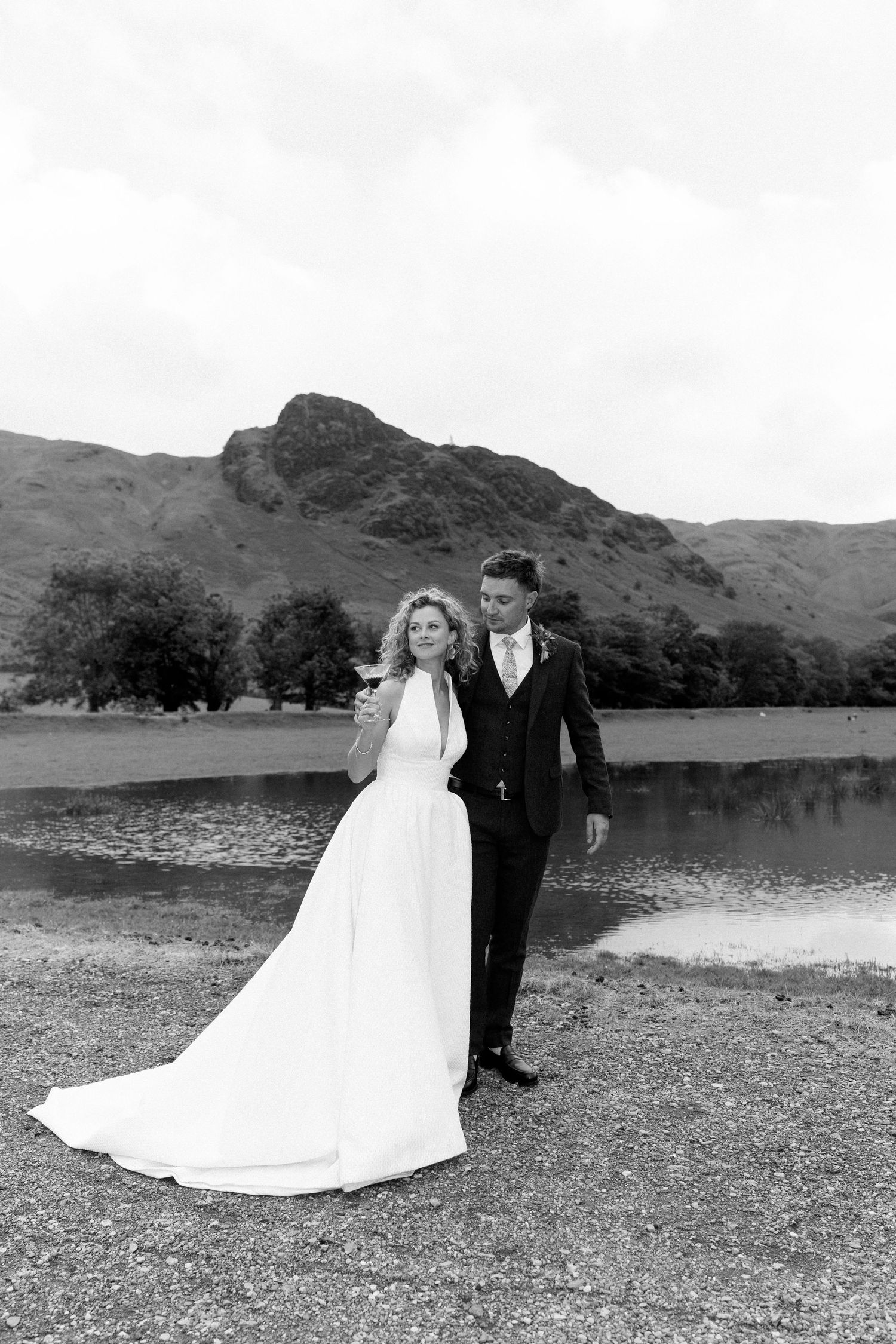 Black and white wedding portraits by a lake with mountains in background.