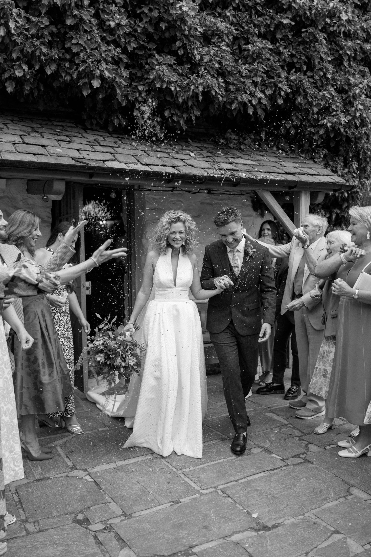 Wedding celebration with guests and wedding party outside rustic stone building.