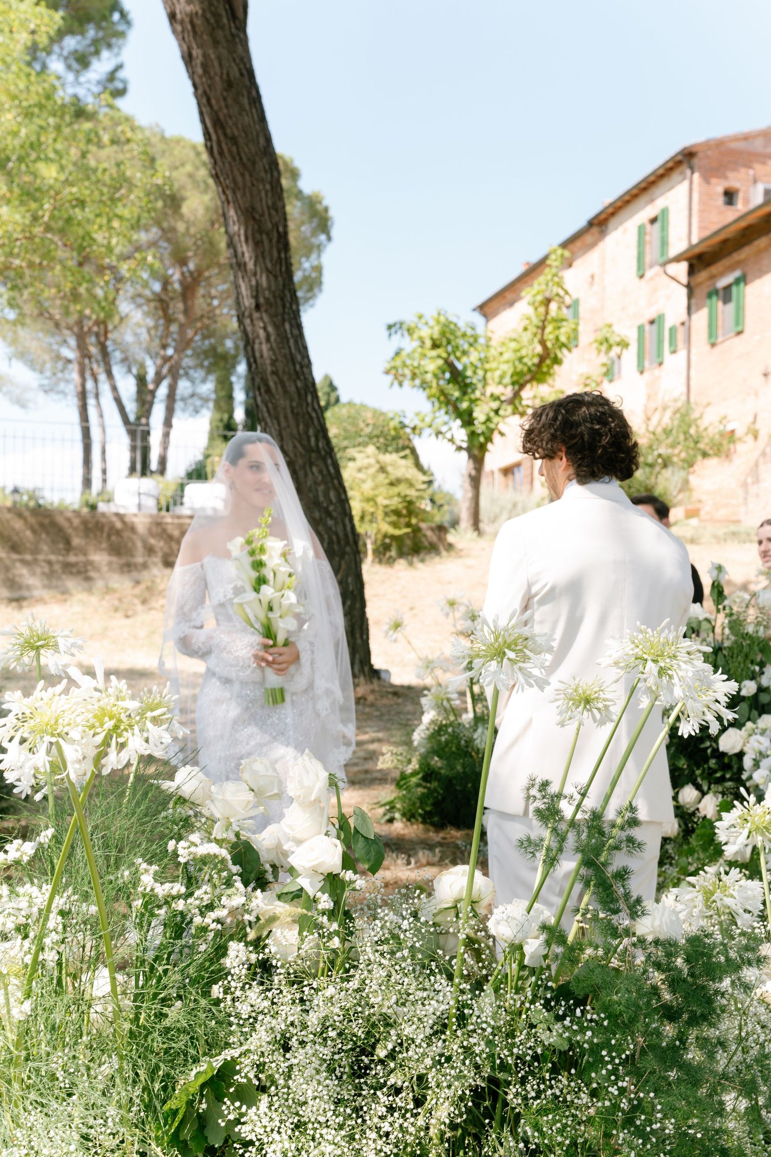 White floral arrangements and delicate greenery line a garden pathway near a Mediterranean-style building.