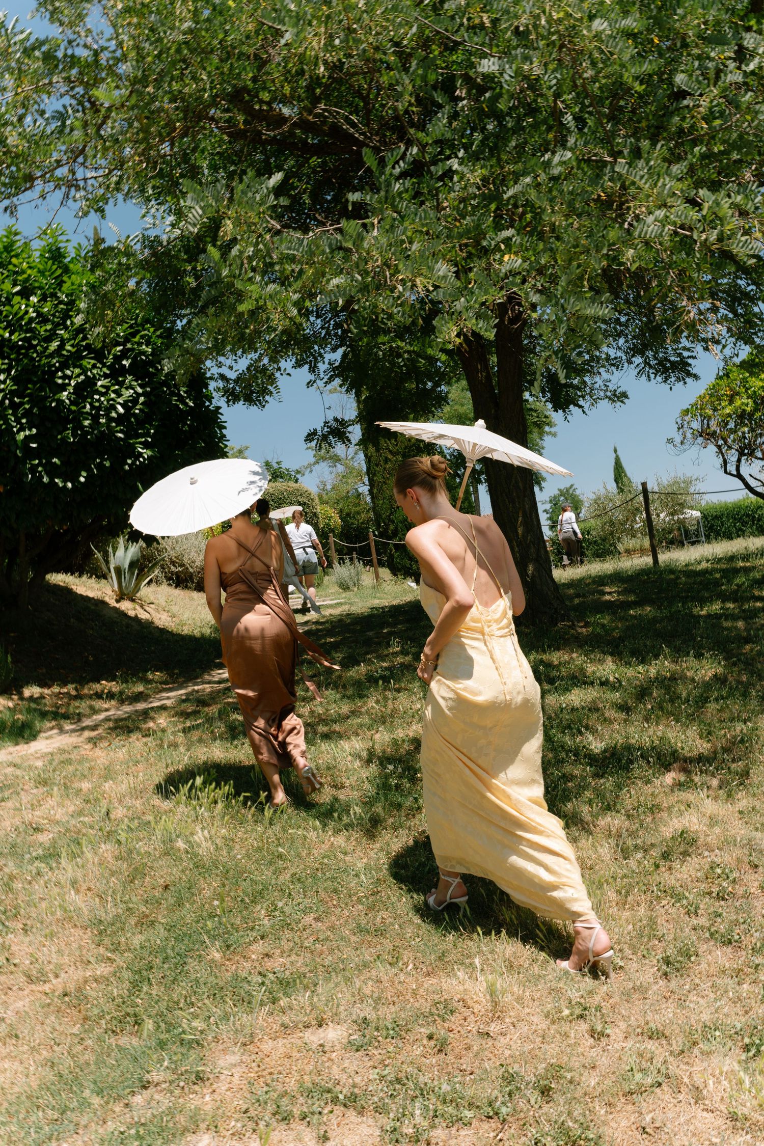 Sequence showing movement in a sunny field with parasols and flowing dresses.