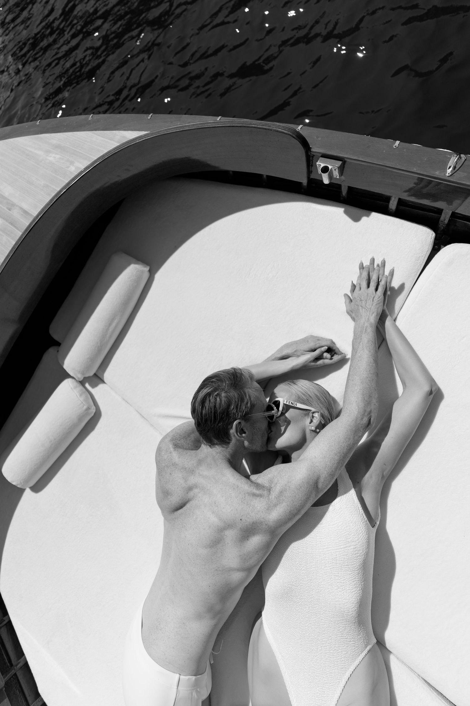 Aerial black and white view of couple embracing on bow of luxury wooden boat at sea.