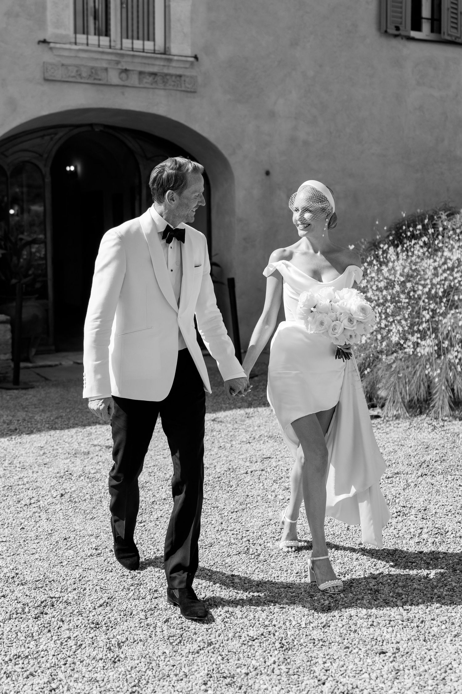 Bride and groom walk hand in hand outside Italian villa in classic black and white wedding photo.