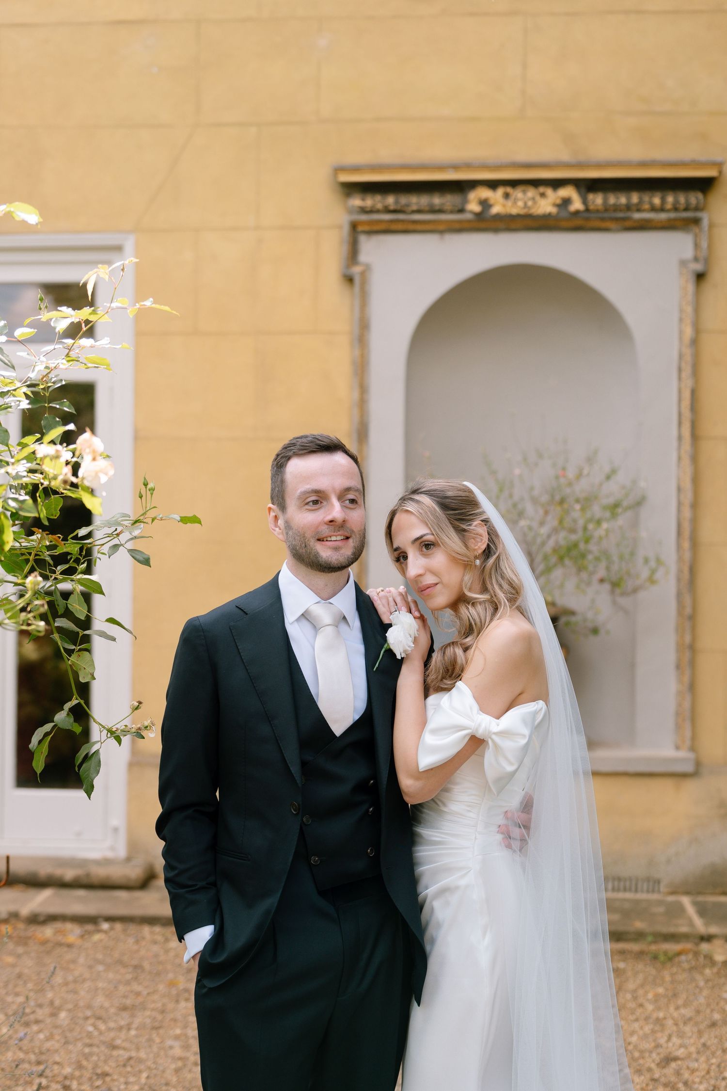 Intimate wedding moment captured outside yellow building with white architectural details.