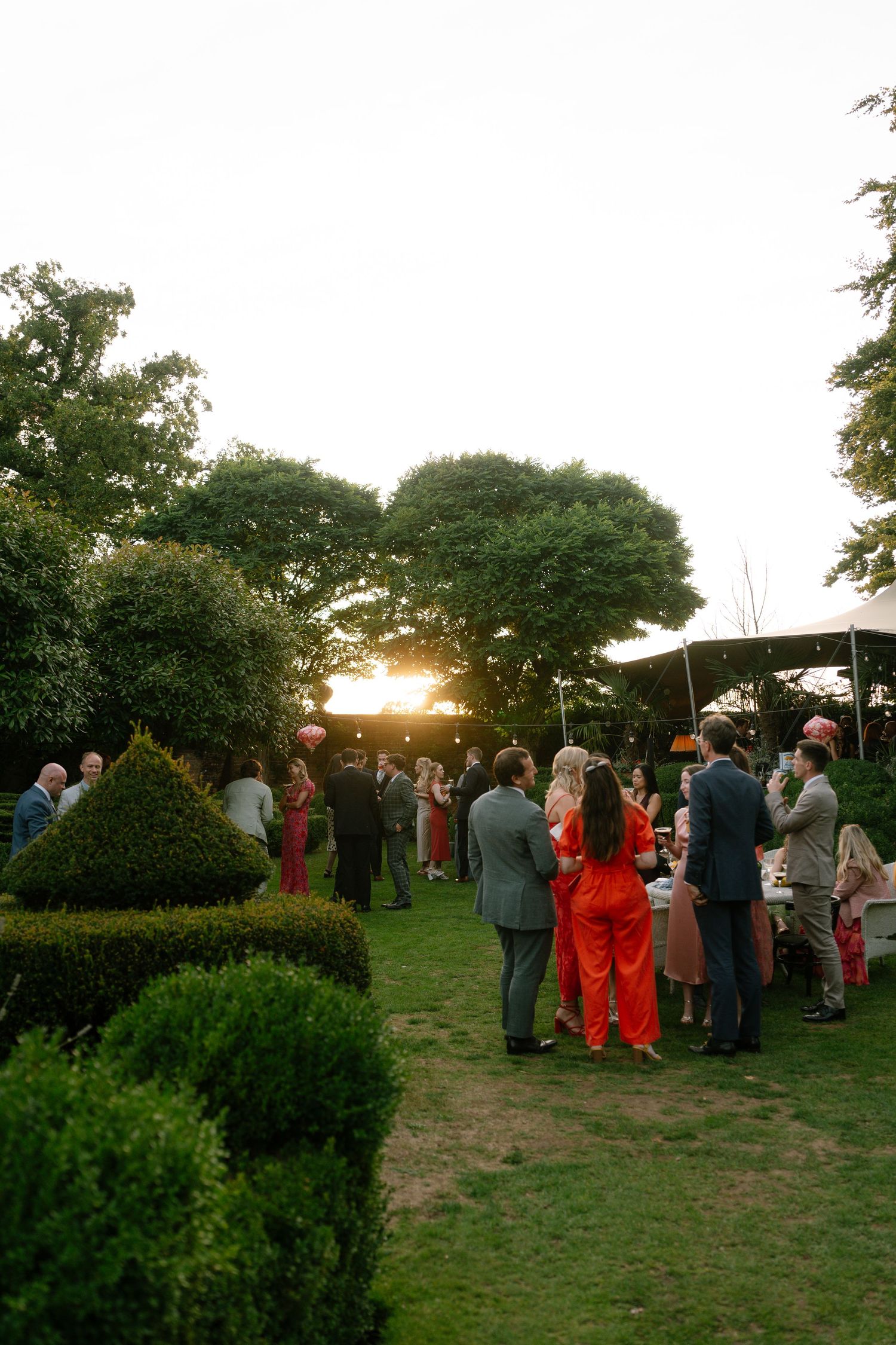 Wedding guests gather on a grassy hill during sunset for an outdoor reception.