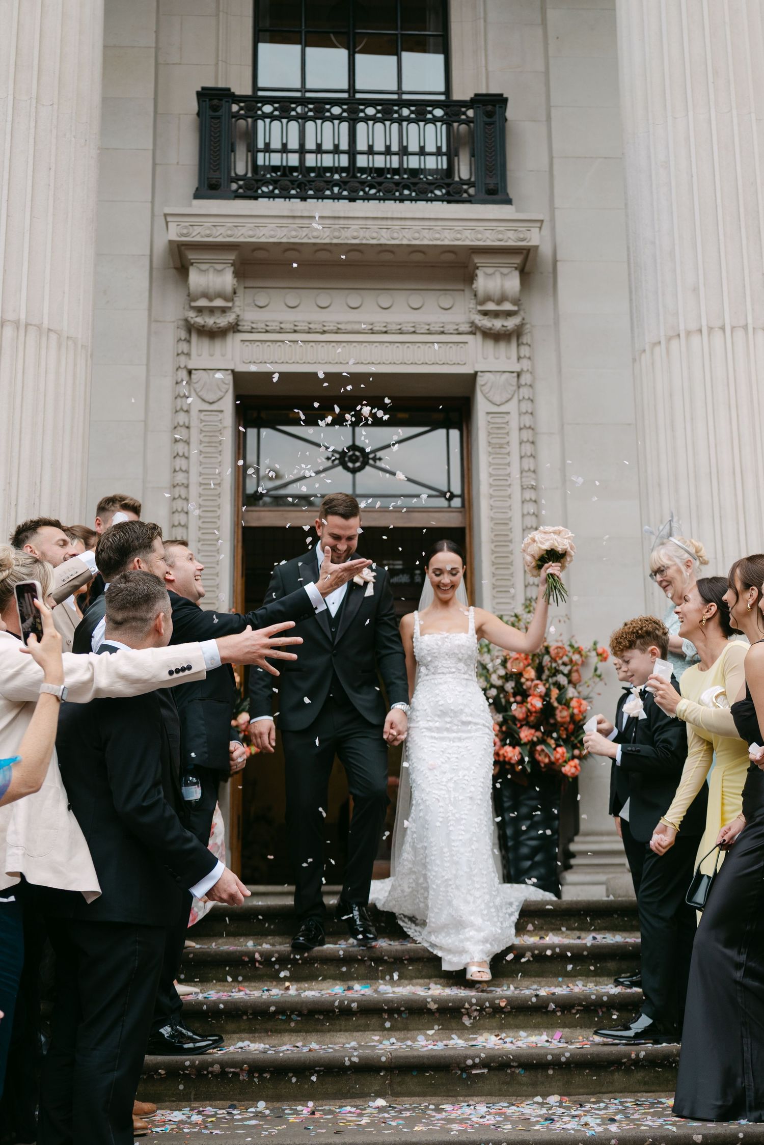 Wedding party celebrates with confetti and dancing on grand steps.