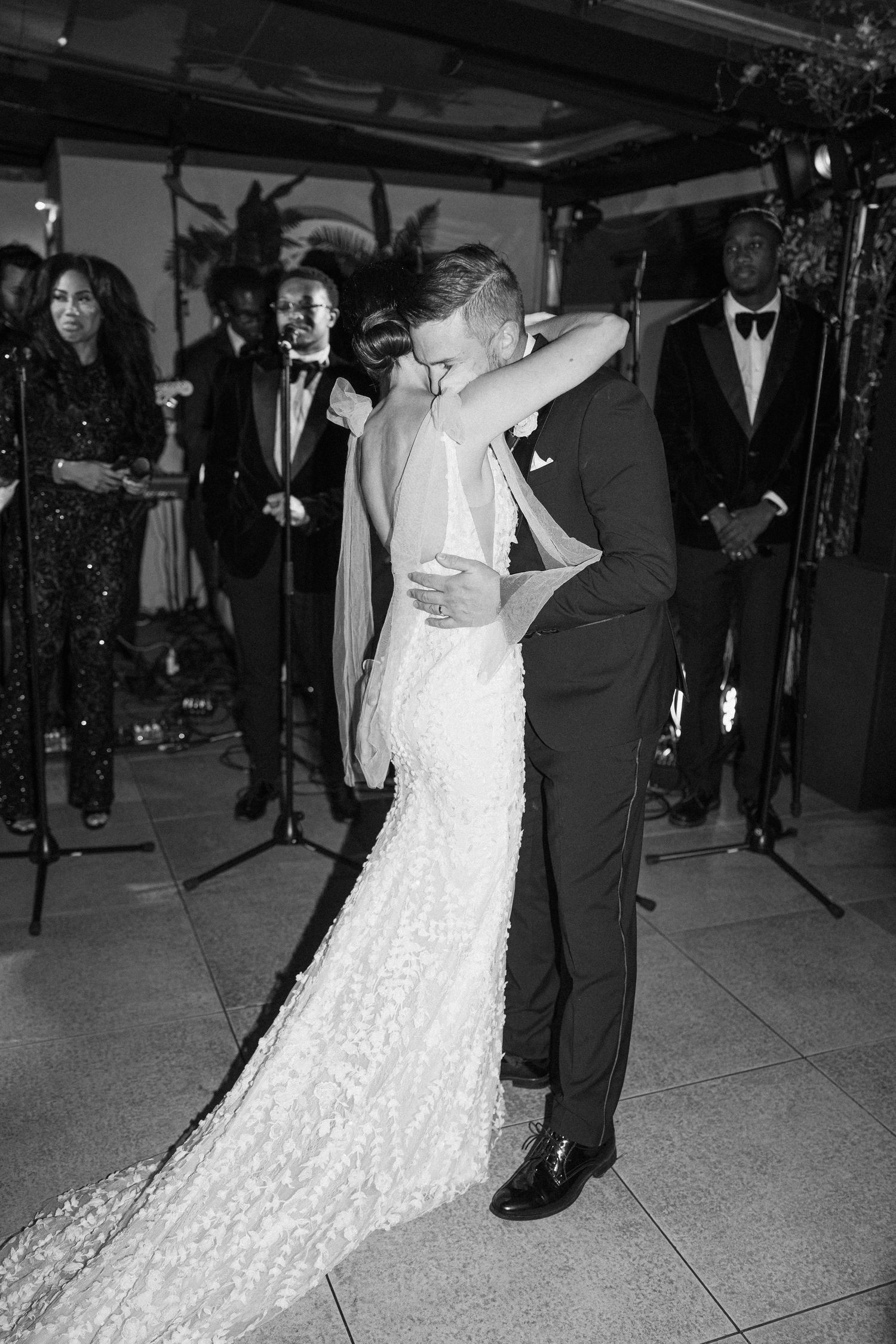 Black and white wedding photo of a couple's intimate dance with band members in background.