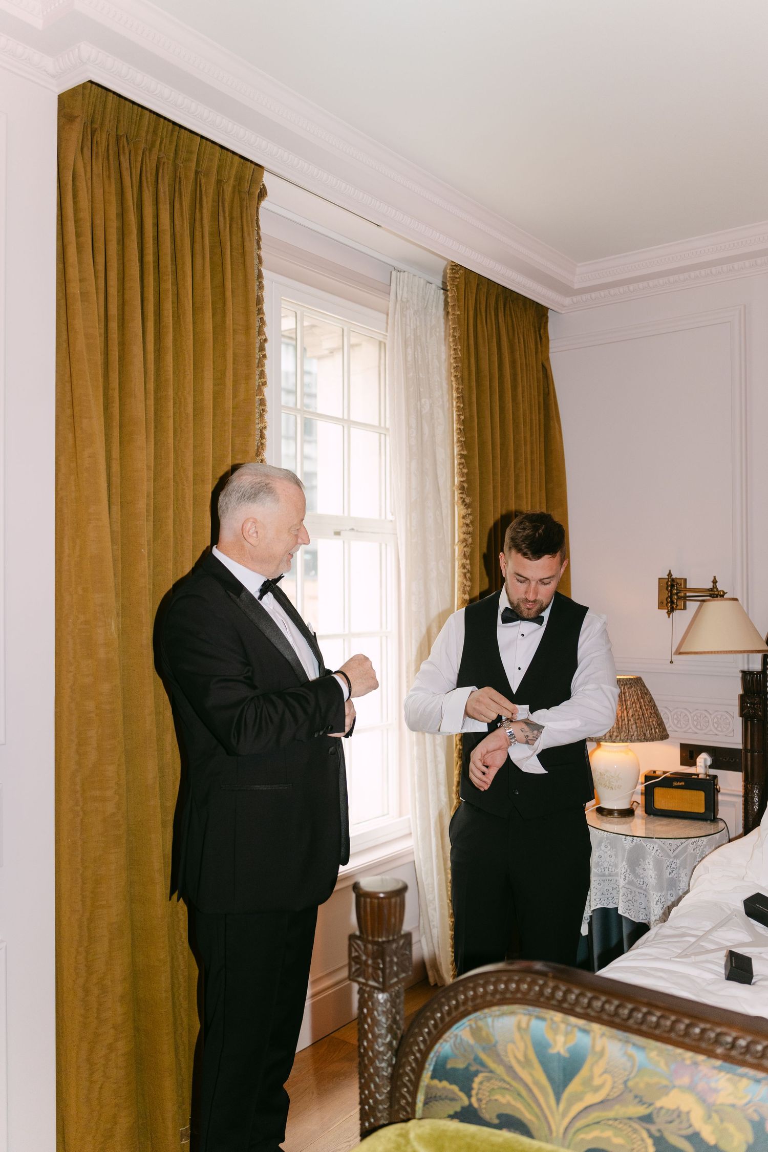 Two people in formal attire check the time in an elegantly decorated room.