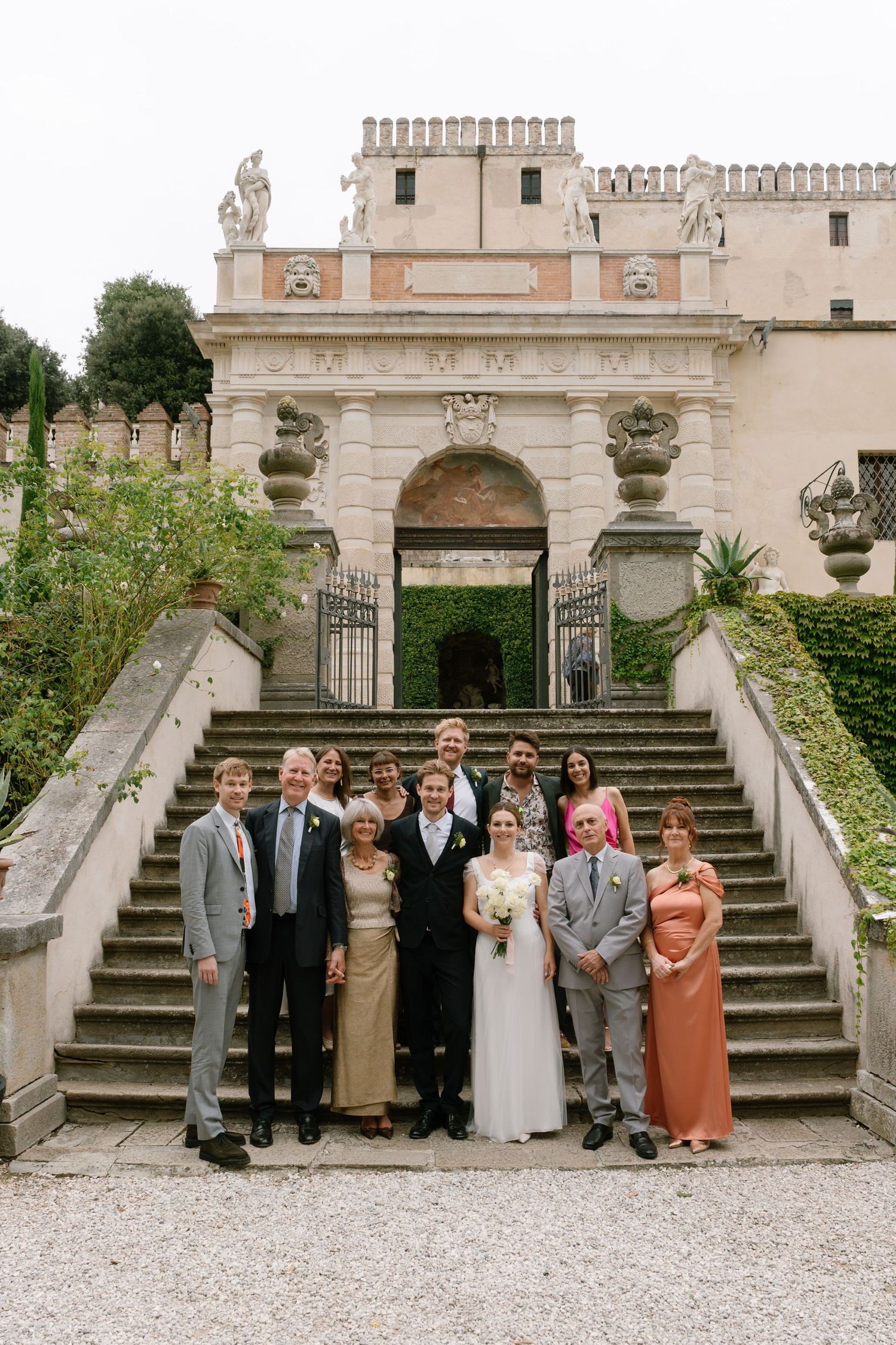 Wedding party poses for formal photos on grand stone steps of a historic building.