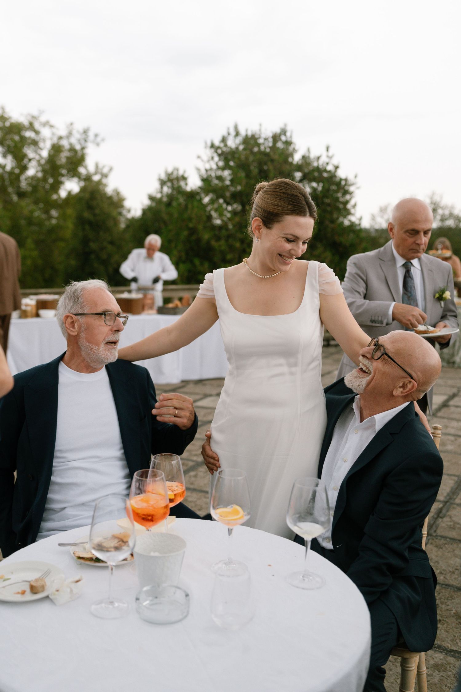 Wedding guests sharing laughter and drinks at an outdoor table.