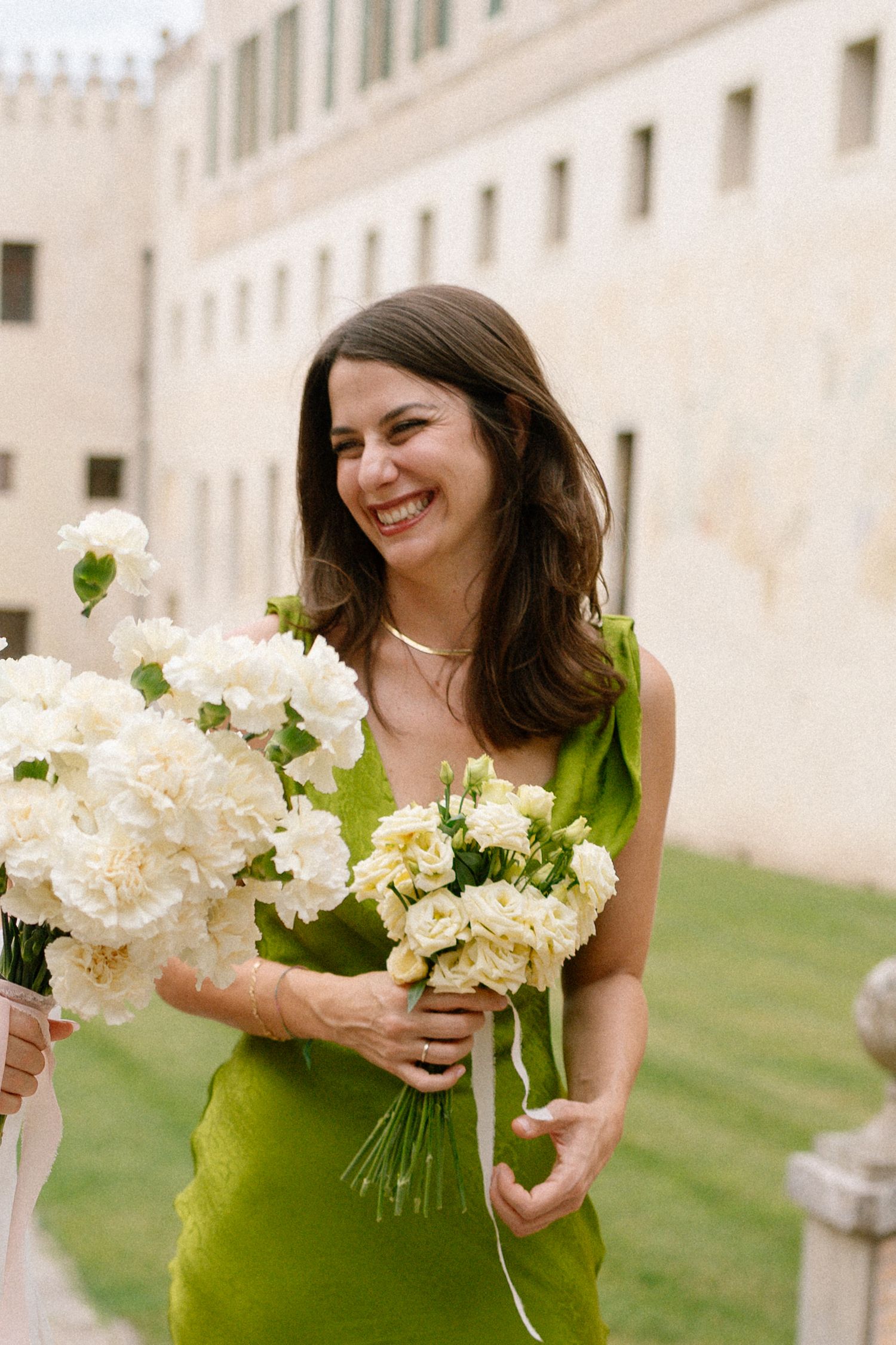 Bridesmaid in green dress holds white floral bouquets against castle backdrop.