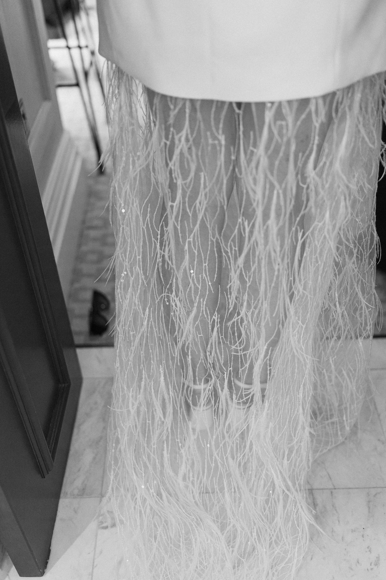 Close-up black and white detail of delicate feather and beaded wedding dress hem.