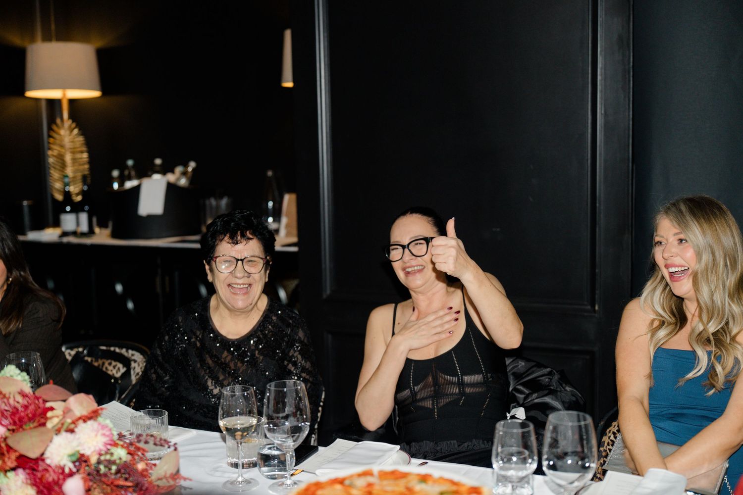 Three women laughing and enjoying themselves at a wedding reception dinner table.