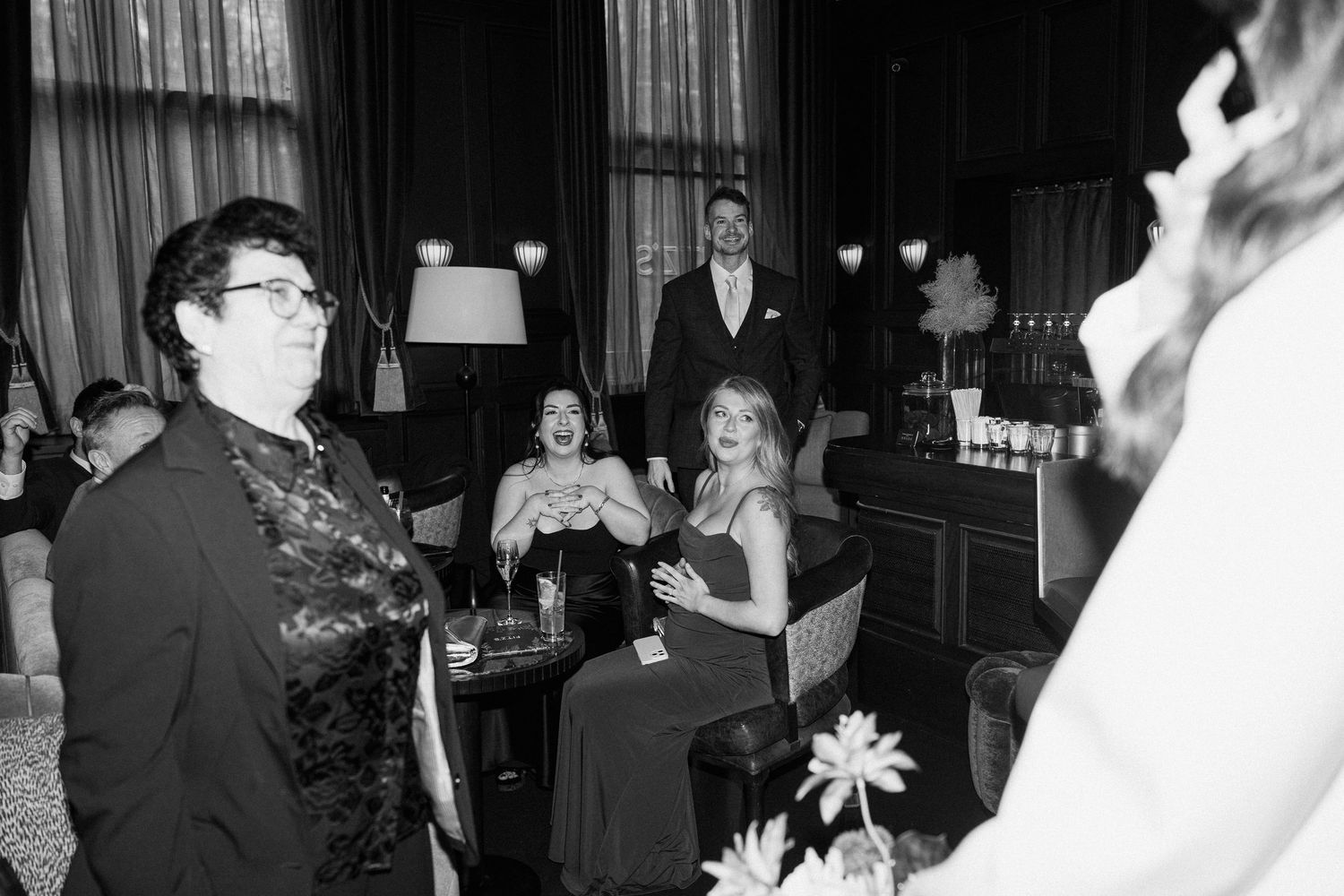Wedding guests socializing in elegant dark-interior bar during black and white reception.