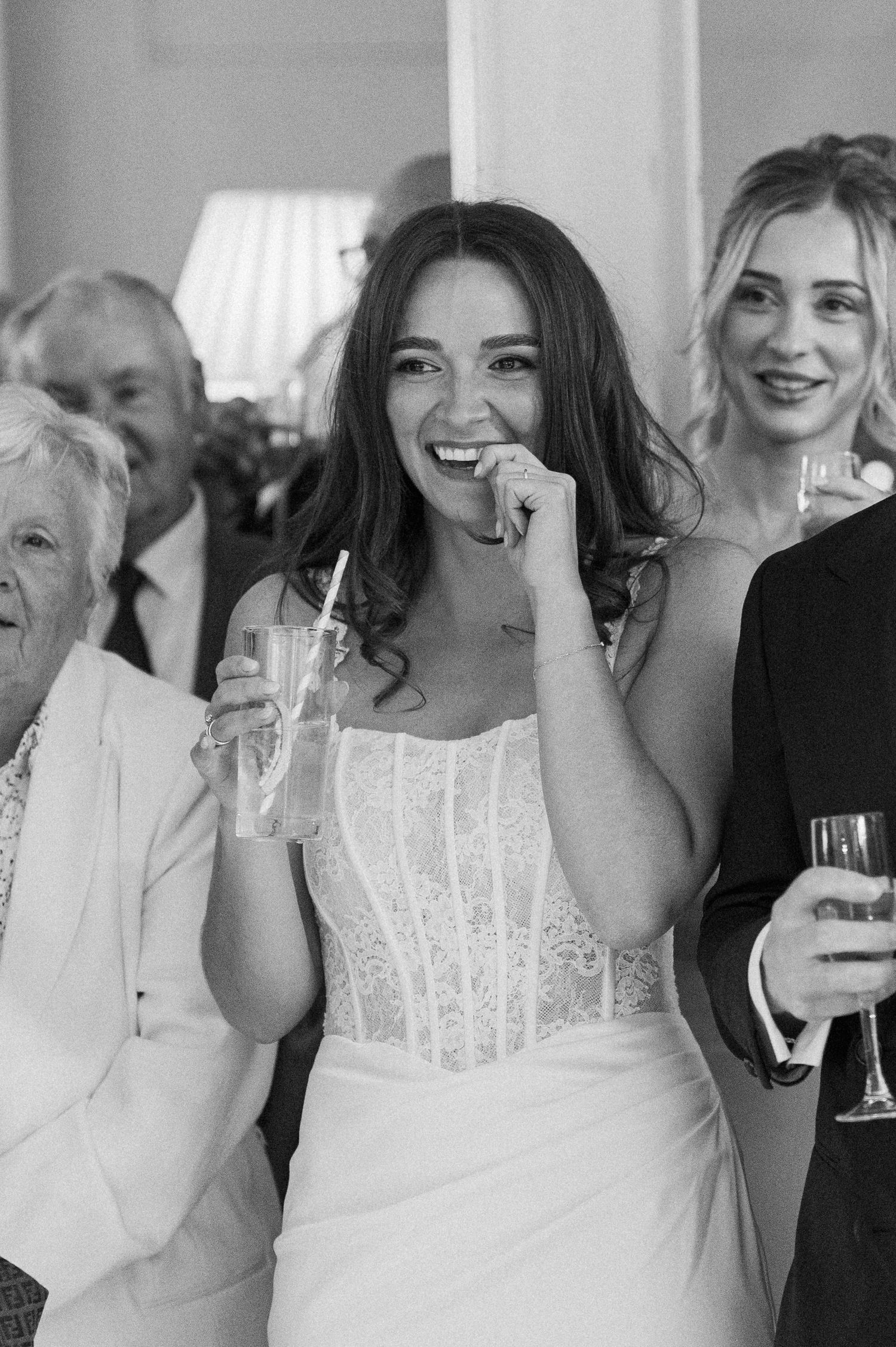 Smiling bride in lace corset wedding dress laughing with guests during wedding reception speeches.