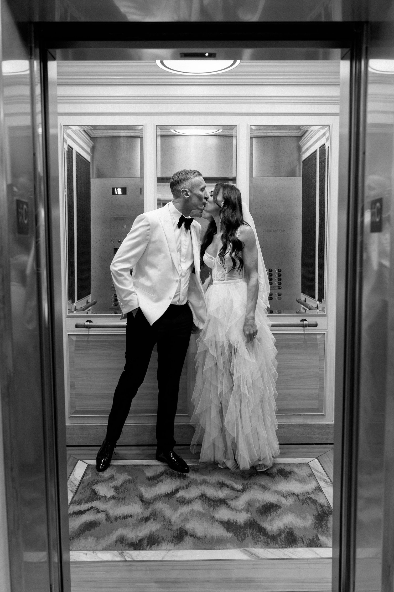 Bride and groom create artistic black and white photos in a mirrored hotel corridor.