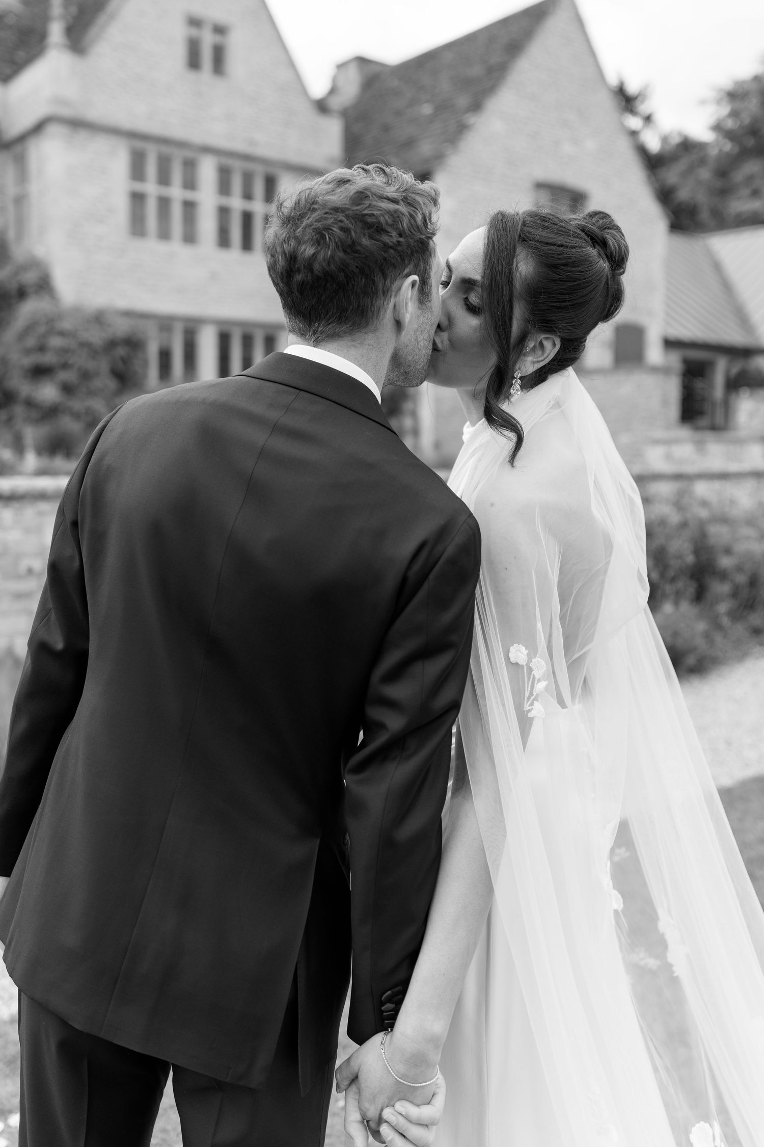 Bride and groom share romantic kiss in black and white portrait outside stone wedding venue.