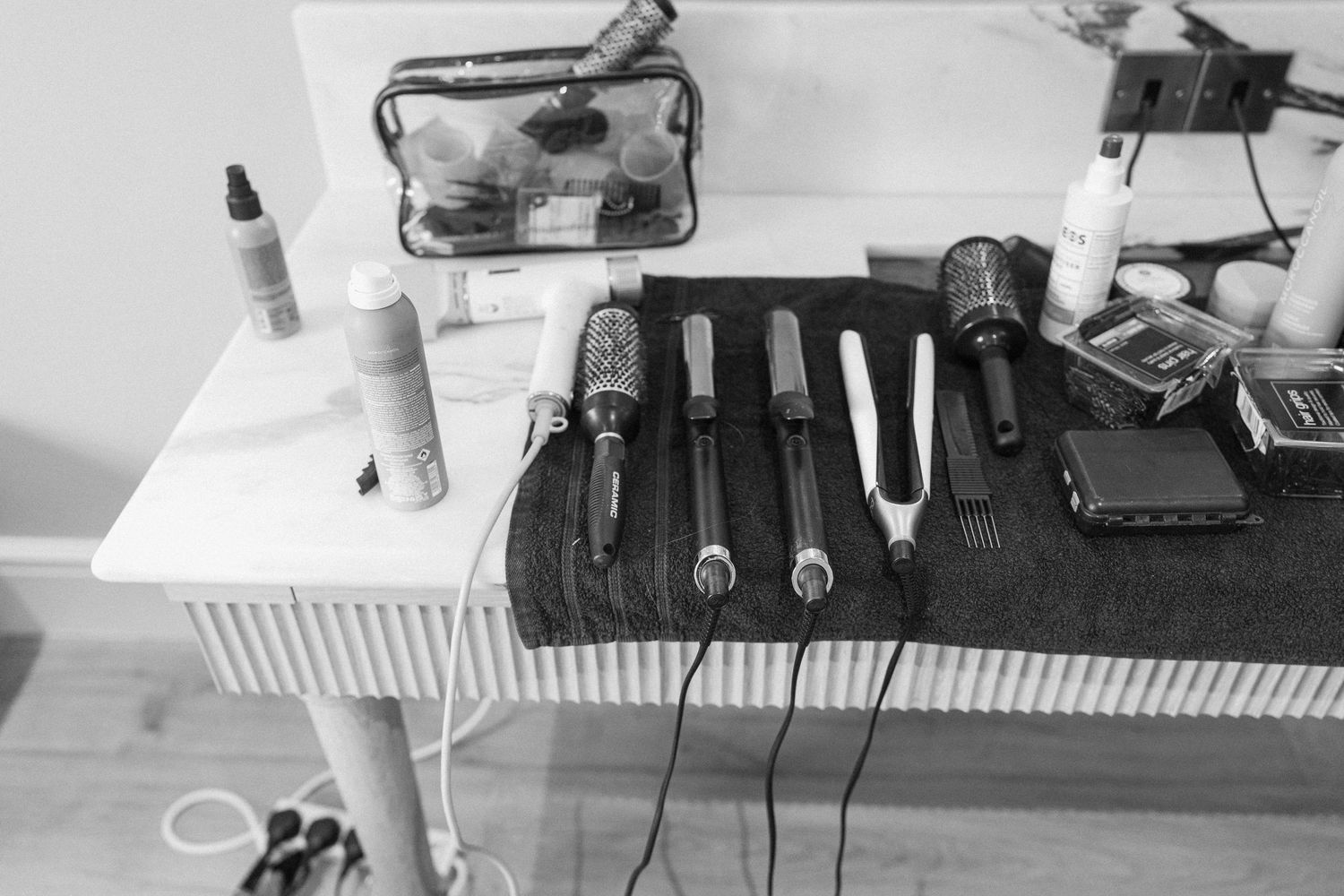 Black and white flat lay of hair styling tools and products arranged on a white table.