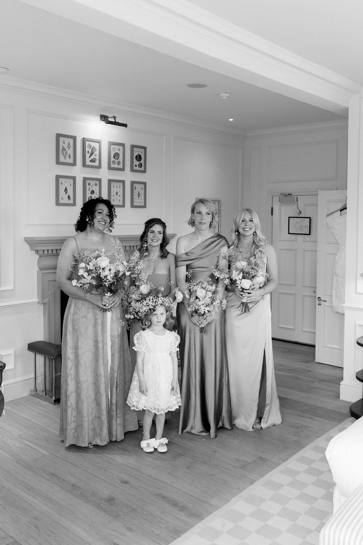 Four bridesmaids in gold dresses with flower girl holding bouquets in black and white photo.